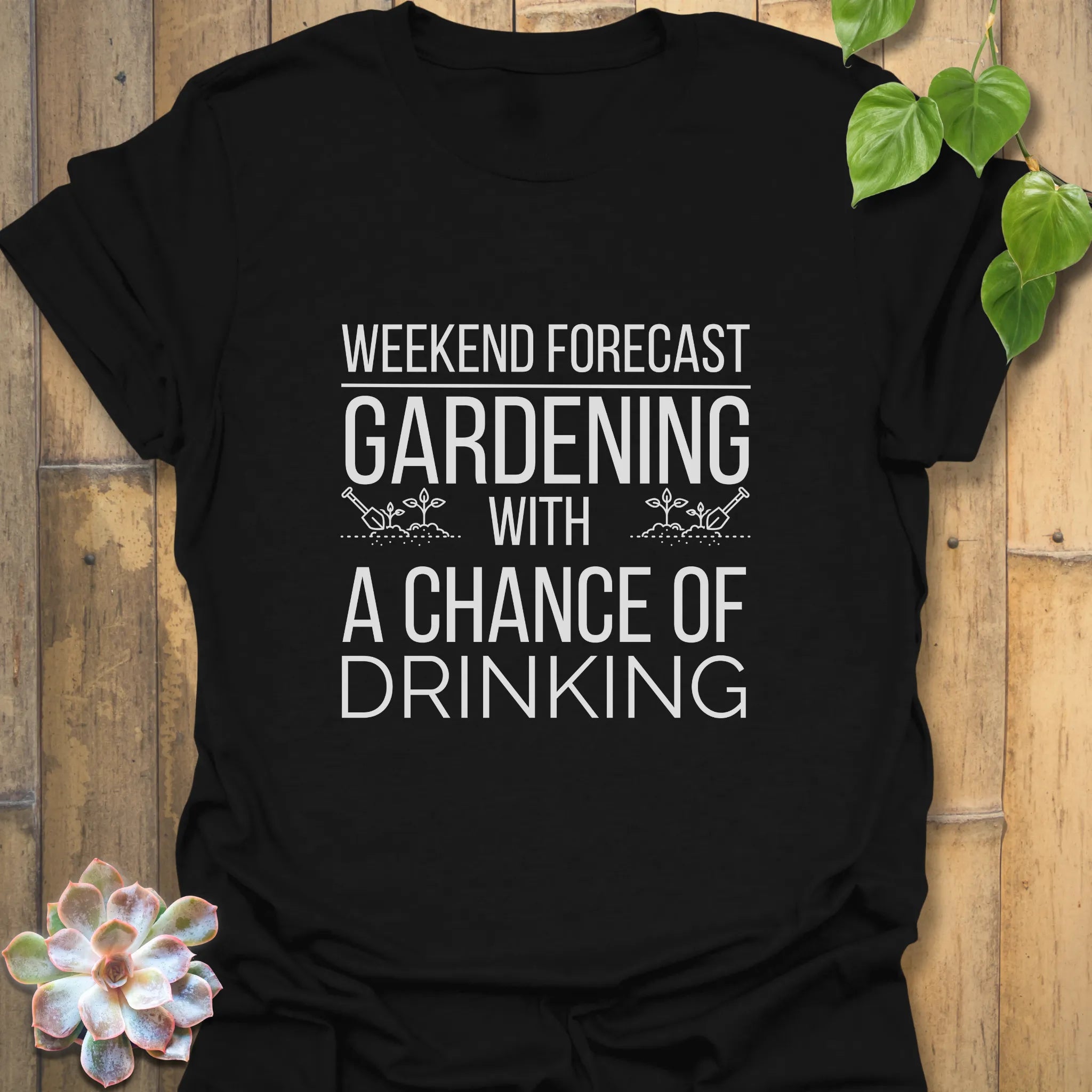 Black unisex T-shirt with white typography reading “Gardening solves most of my problems, wine solves the rest,” displayed flat with a succulent on the side.