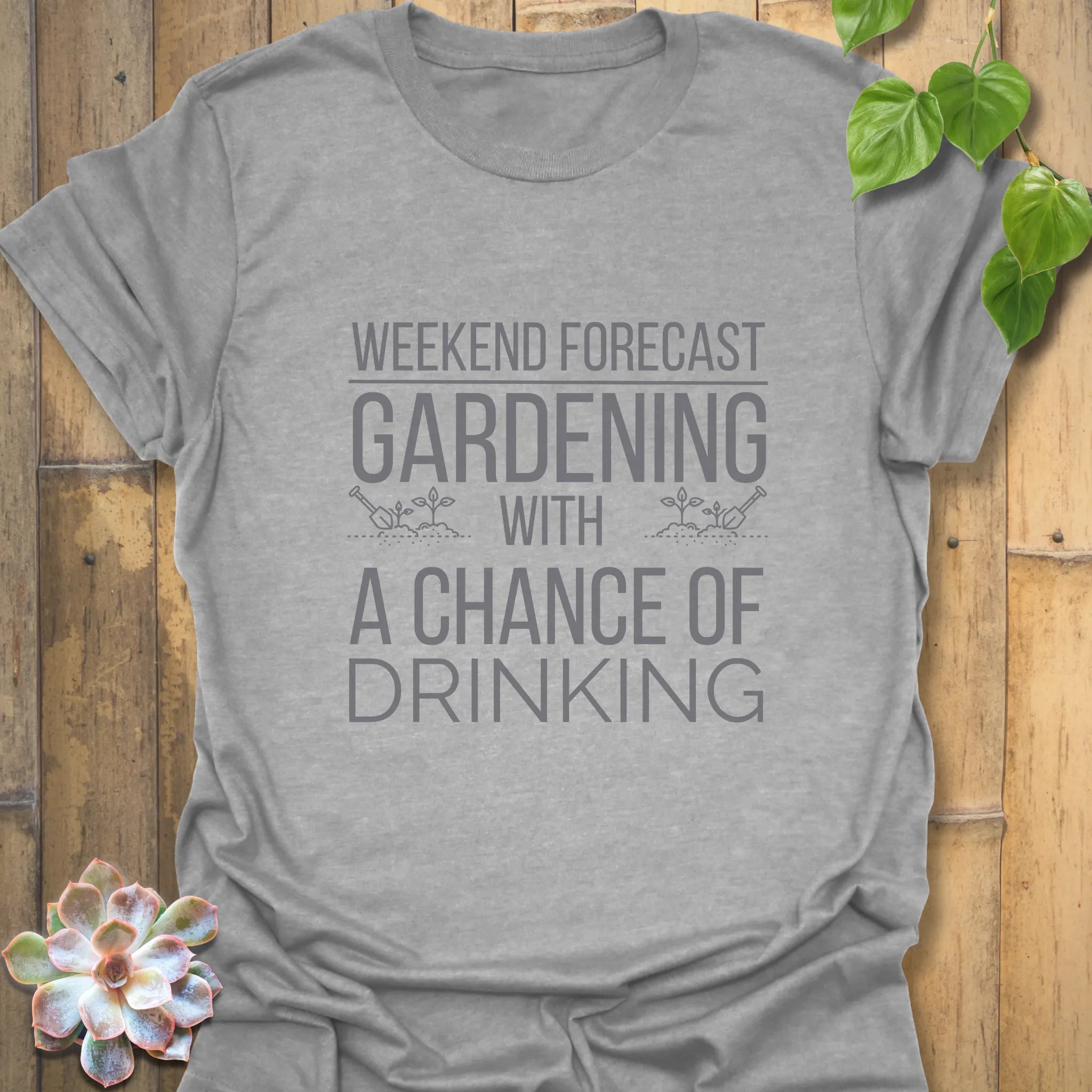 Sport grey cotton T-shirt with bold white lettering saying “Gardening solves most of my problems, wine solves the rest,” laid flat with a small succulent for decoration.