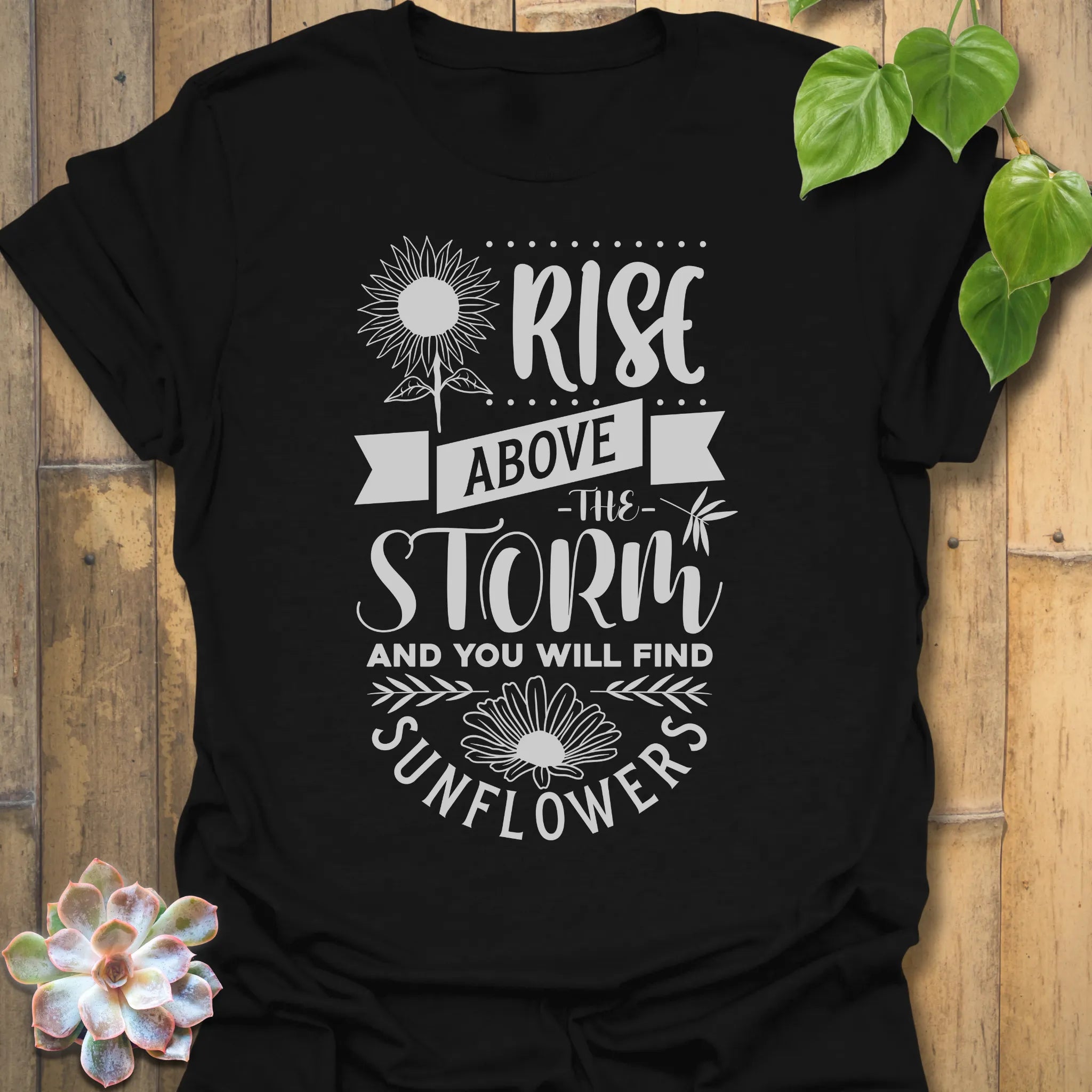 Black t-shirt featuring the design Above The Storm printed in bold letters, floral inspirational sunflower graphic shirt.