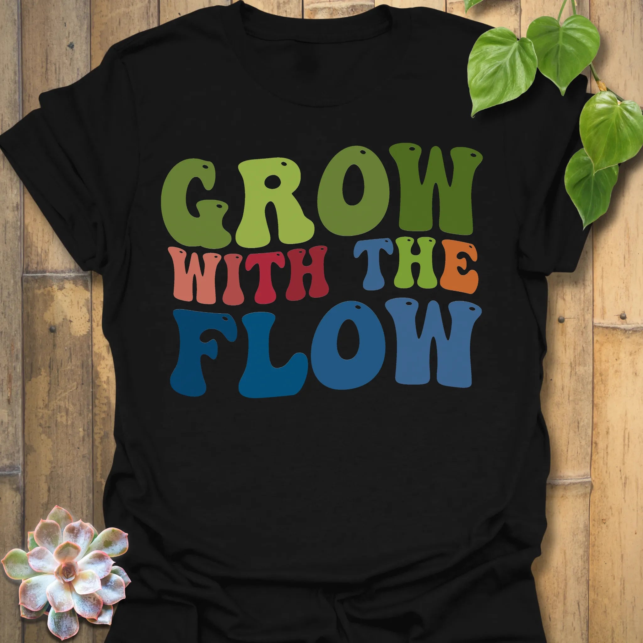 Black t-shirt featuring the design Grow With The Flow printed in bold colorful letters, mindful garden shirt.