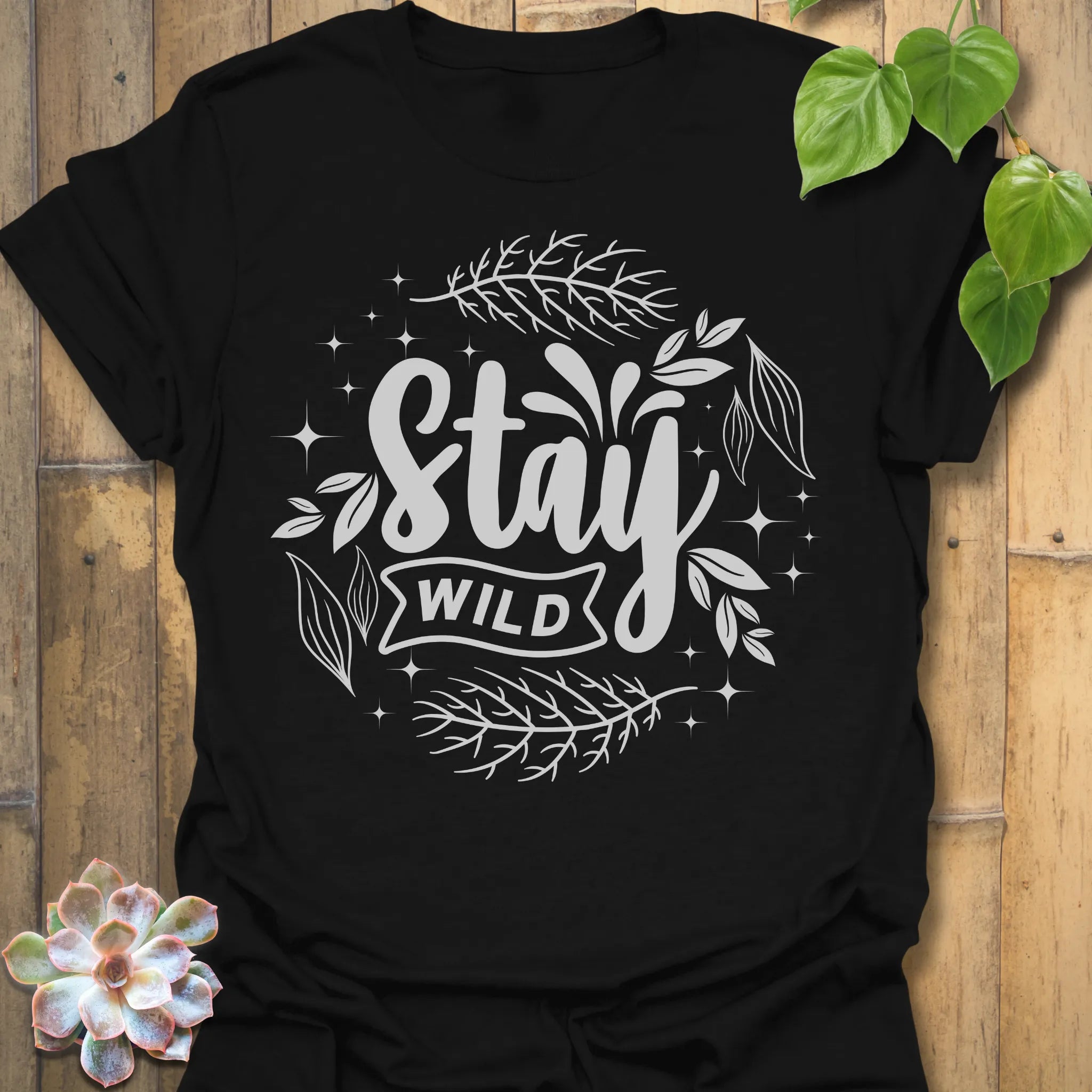 Black t-shirt featuring the design Stay Wild printed in bold white letters, floral graphic lover shirt.