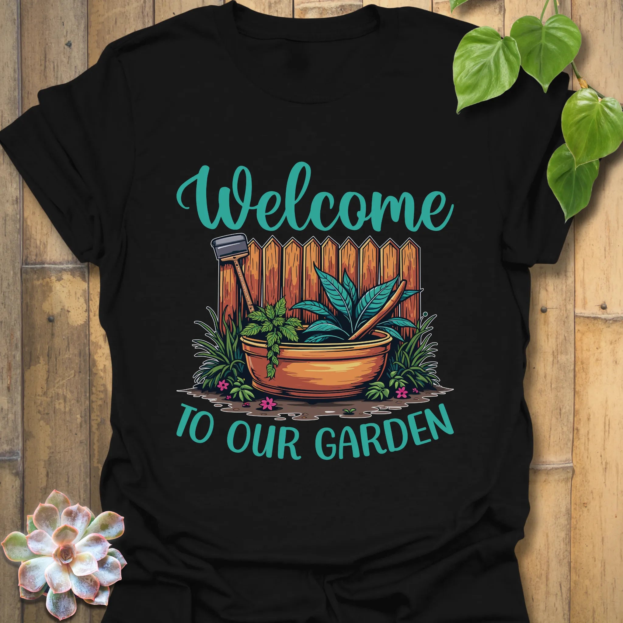 Black t-shirt featuring the design Welcome to our garden with a garden scene, potted plant, and tools, a bold plant lover t-shirt for gardeners and nature fans.