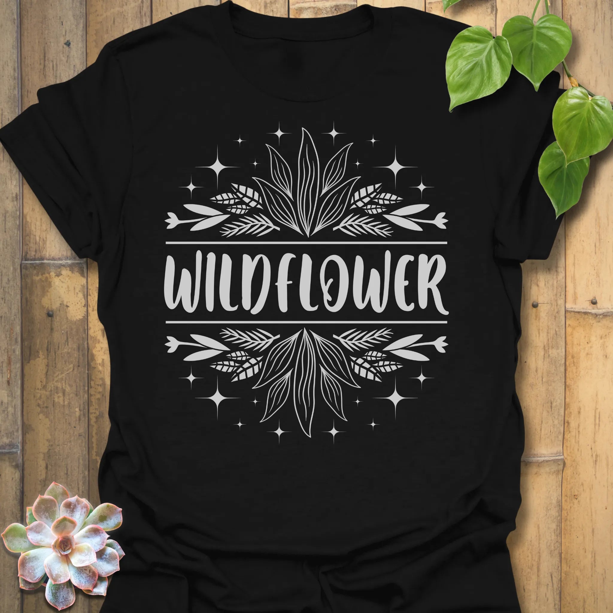 Black t-shirt featuring the design Wildflower printed in bold white letters, floral graphic shirt.