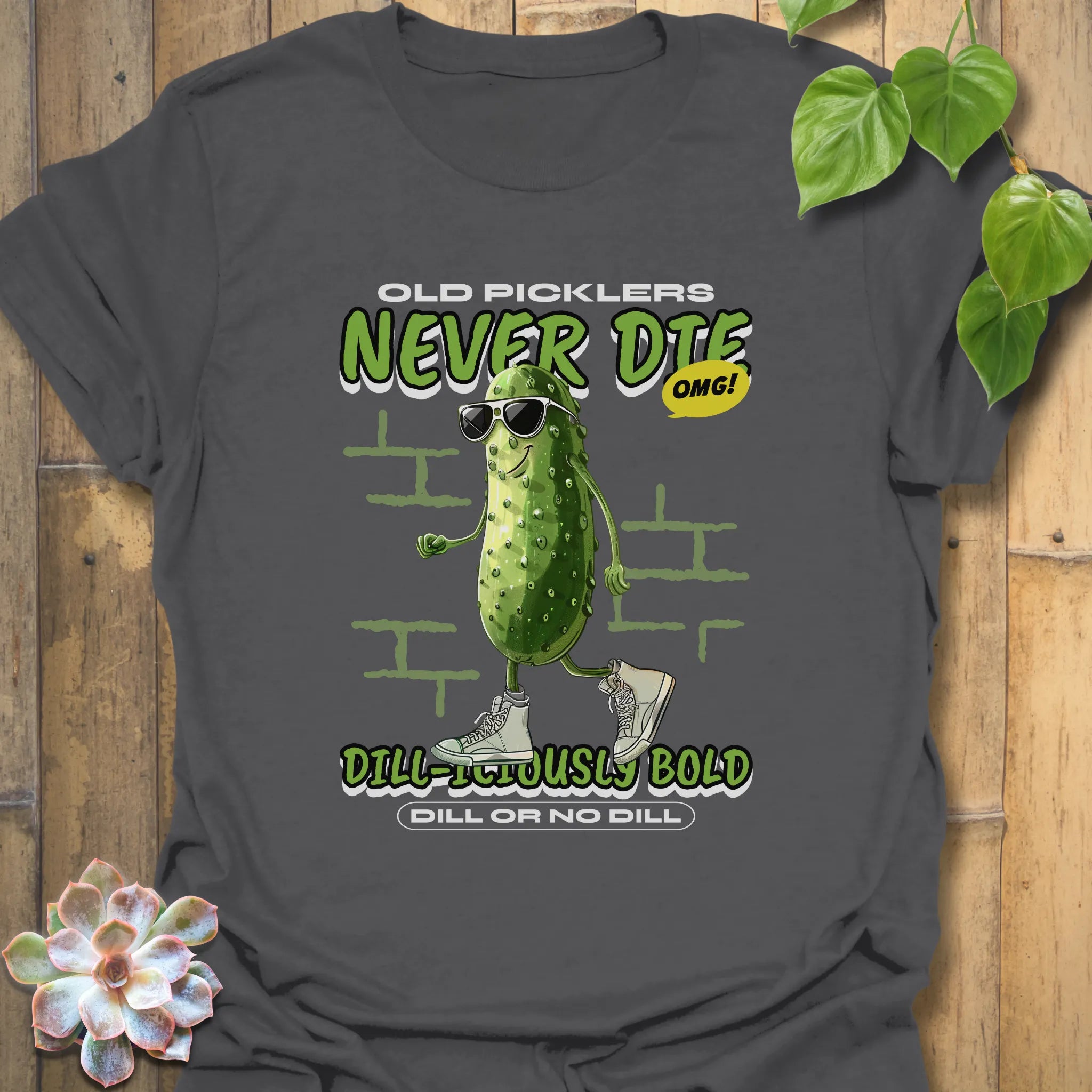 Charcoal grey t-shirt featuring the text “Old Pickles Never Die Dill-Iliously Bold” with a cucumber character in shades