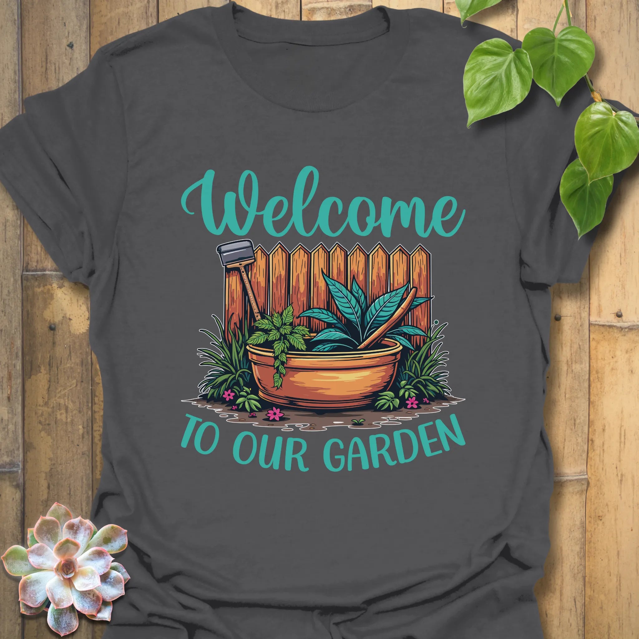 Charcoal t-shirt featuring the design Welcome to our garden with a garden scene, potted plant, and tools, a stylish gardening graphic tee for everyday wear.