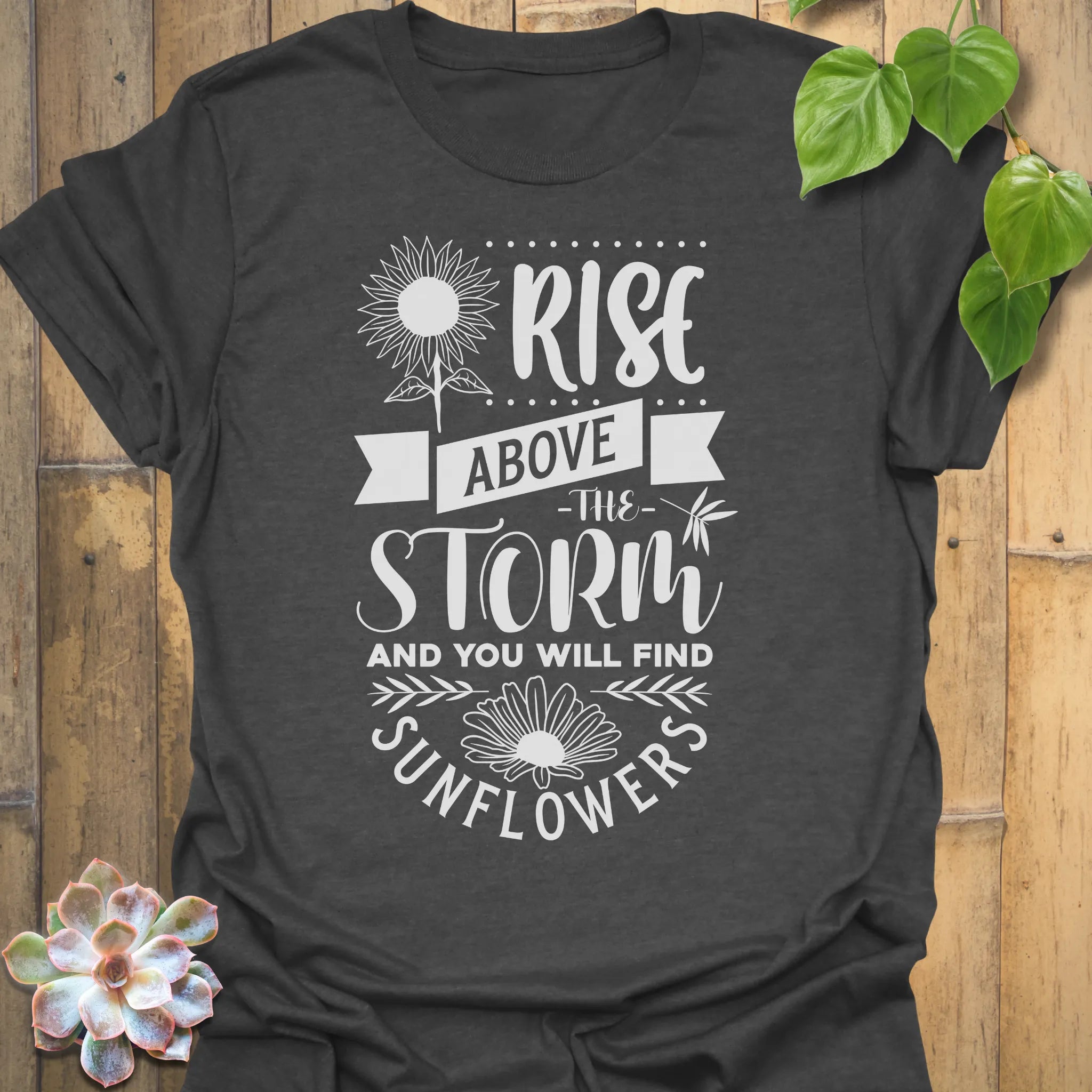 Dark Heather t-shirt featuring the design Above The Storm printed in bold letters, floral inspirational sunflower graphic shirt.