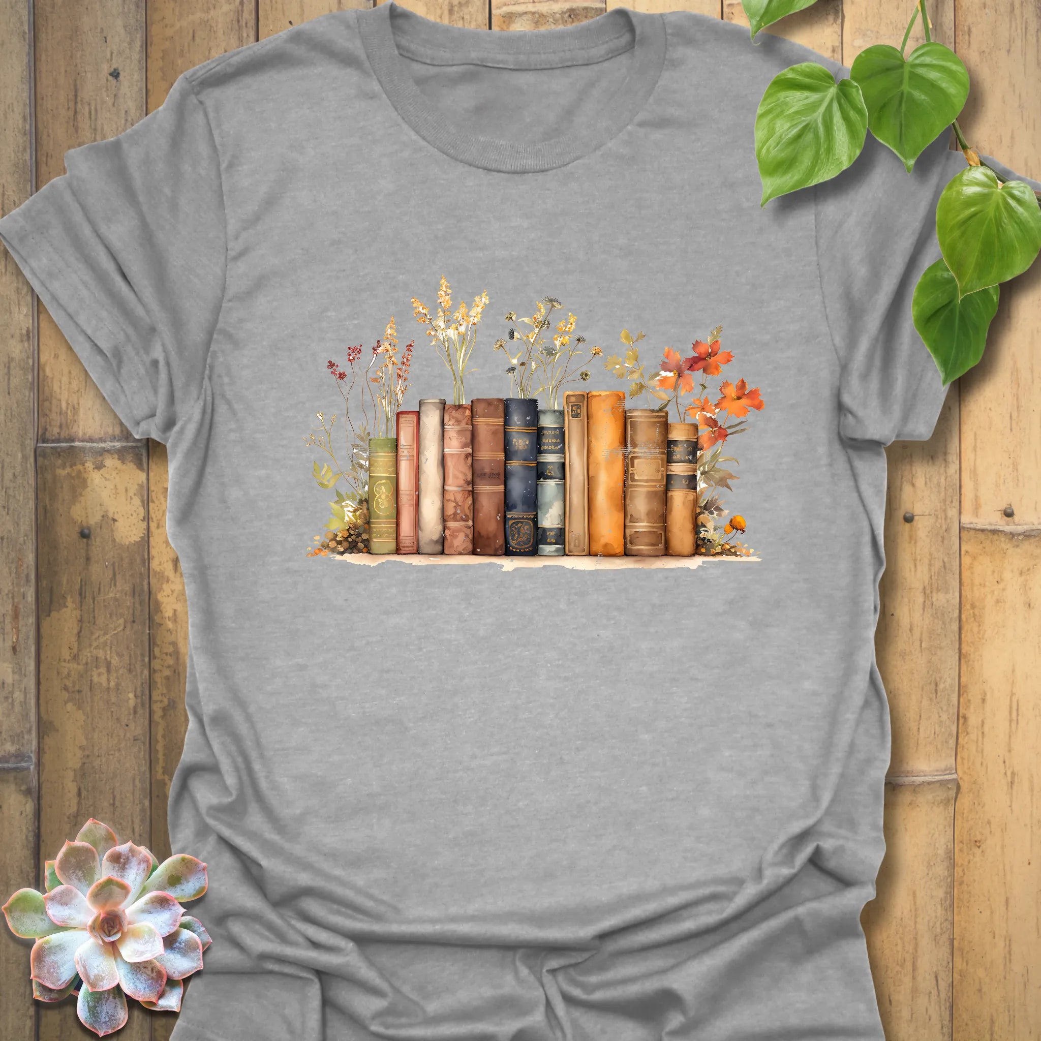 Sport grey “Wildflower Library” tee with a detailed stack of vintage books surrounded by wildflowers — soft, breathable Gildan cotton blend.