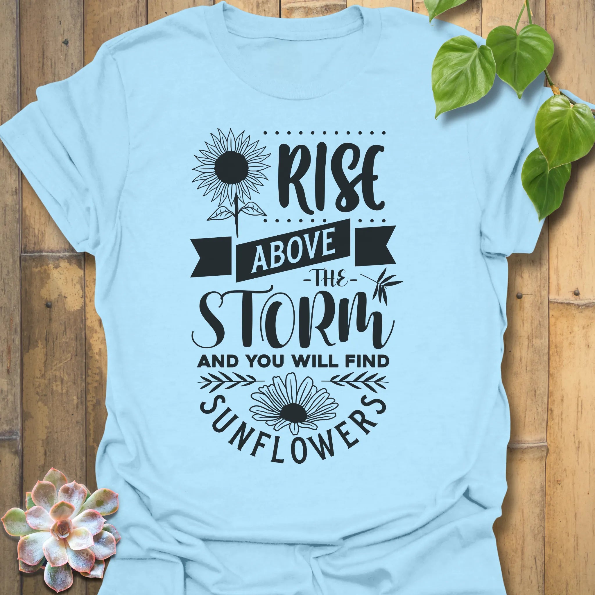 Light Blue t-shirt featuring the design Above The Storm printed in bold letters, floral inspirational sunflower graphic shirt.