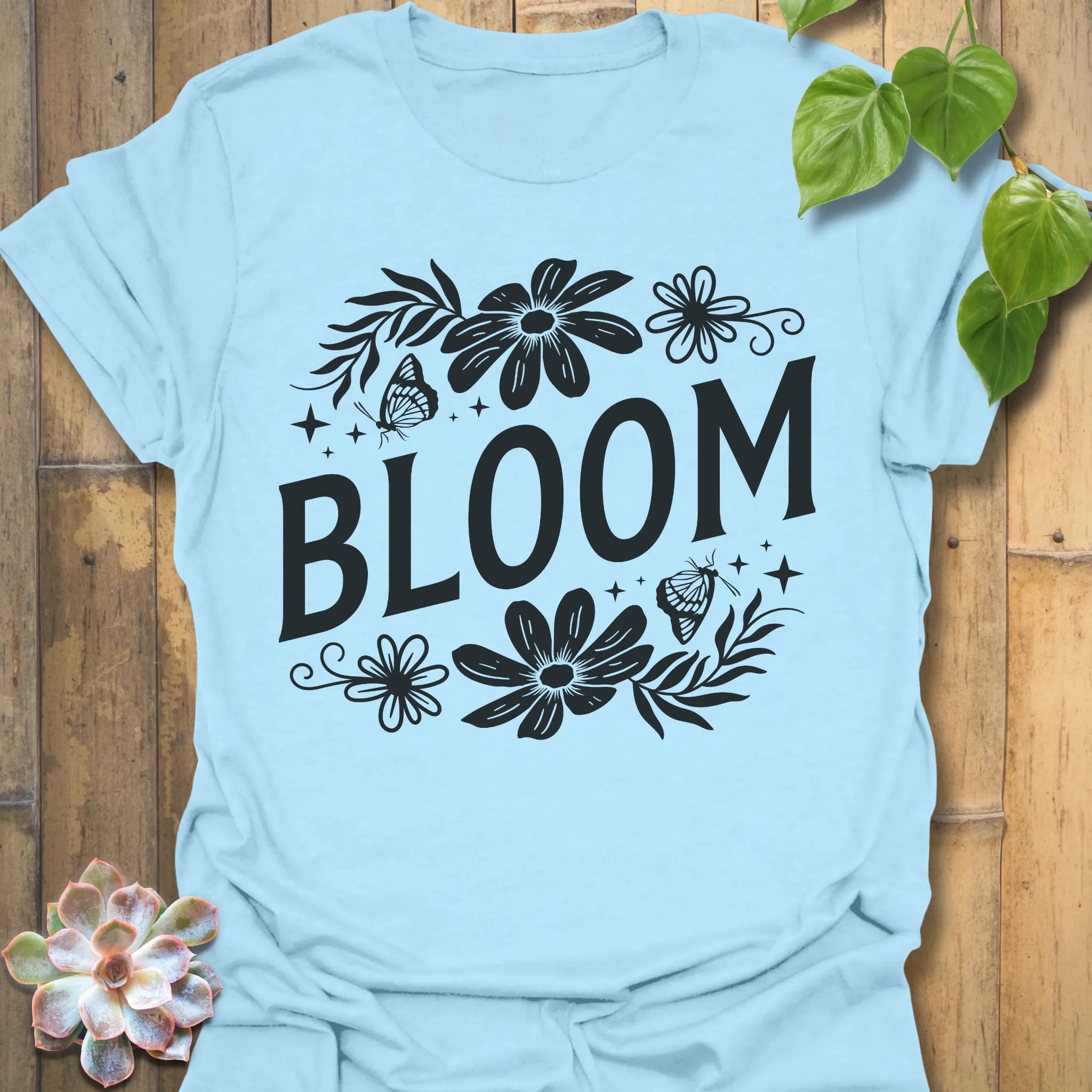 Light Blue t-shirt featuring the design Bloom printed in bold black letters, floral graphic tee for plant lovers.