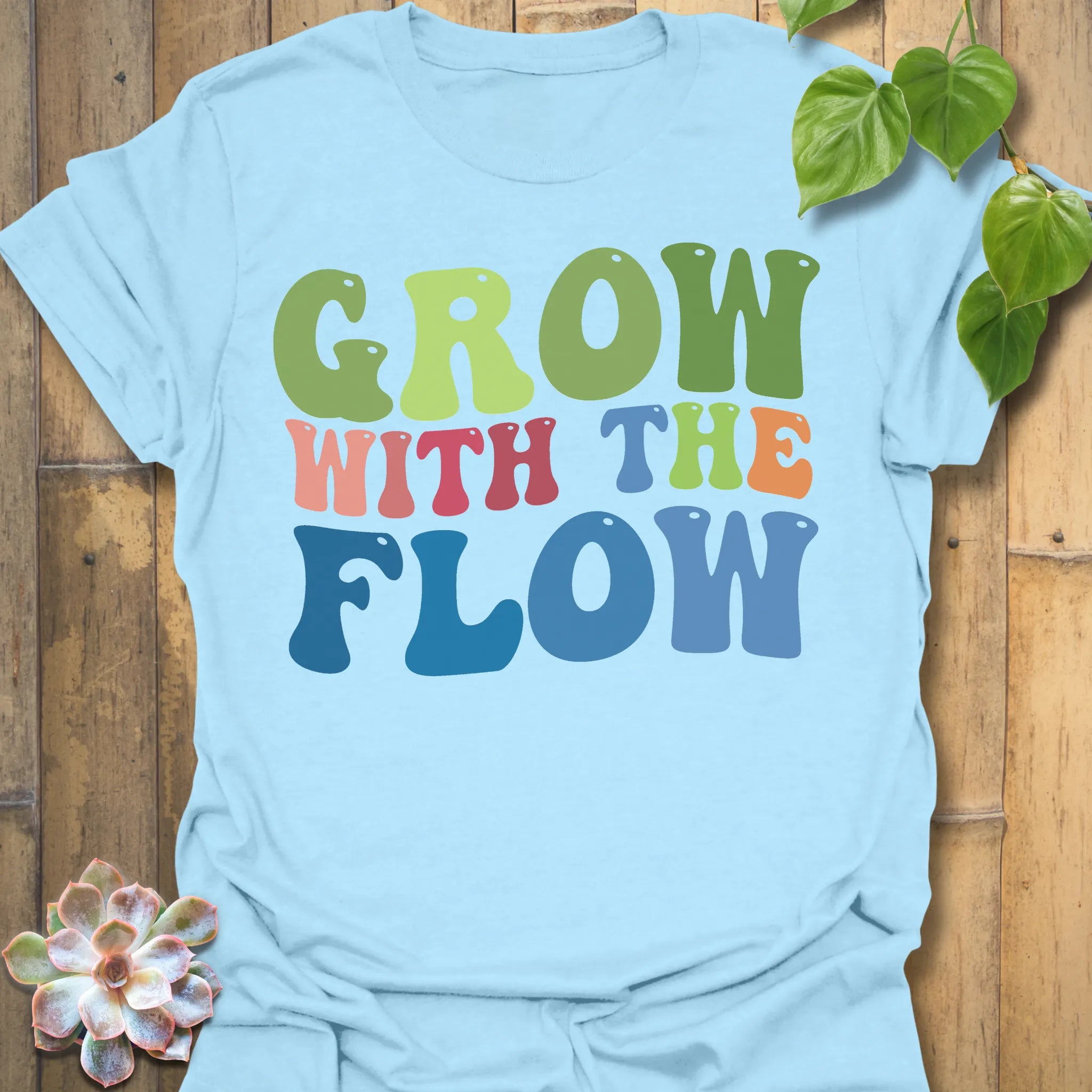 Light Blue t-shirt featuring the design Grow With The Flow printed in bold colorful letters, mindful garden shirt.