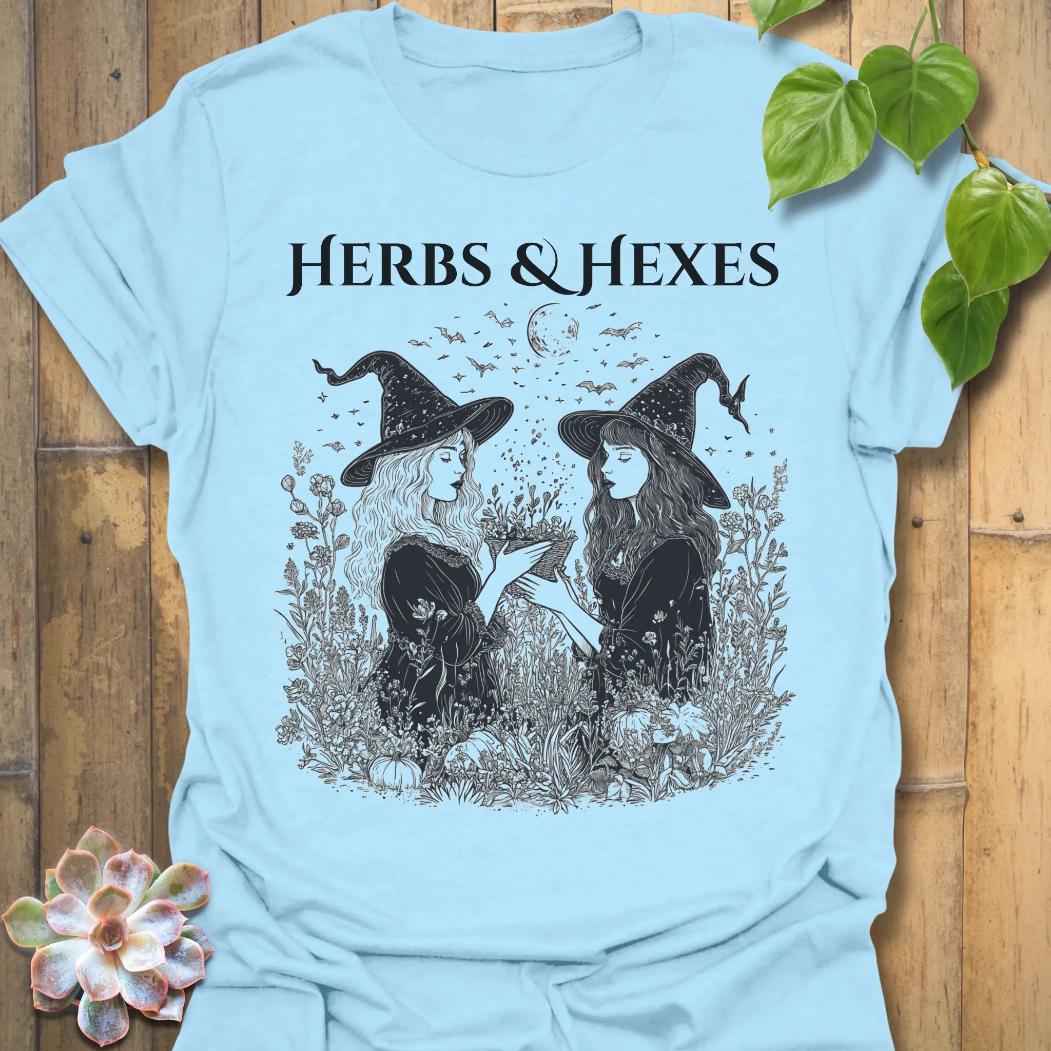 Light Blue t-shirt featuring the design Herbs & Hexes printed in bold black letters, botanical witch t-shirt.