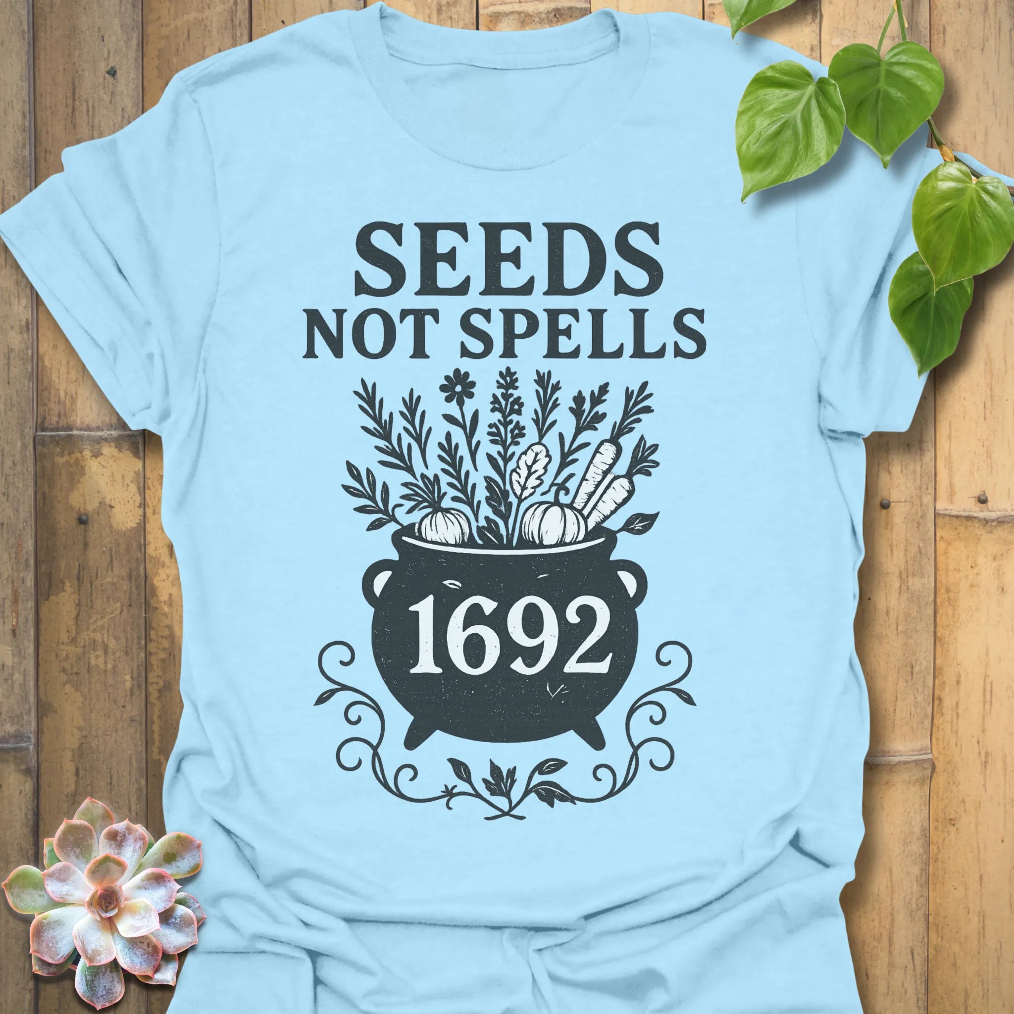 Light Blue t-shirt featuring the design Seeds Not Spells printed in bold letters, halloween plant lover shirt.