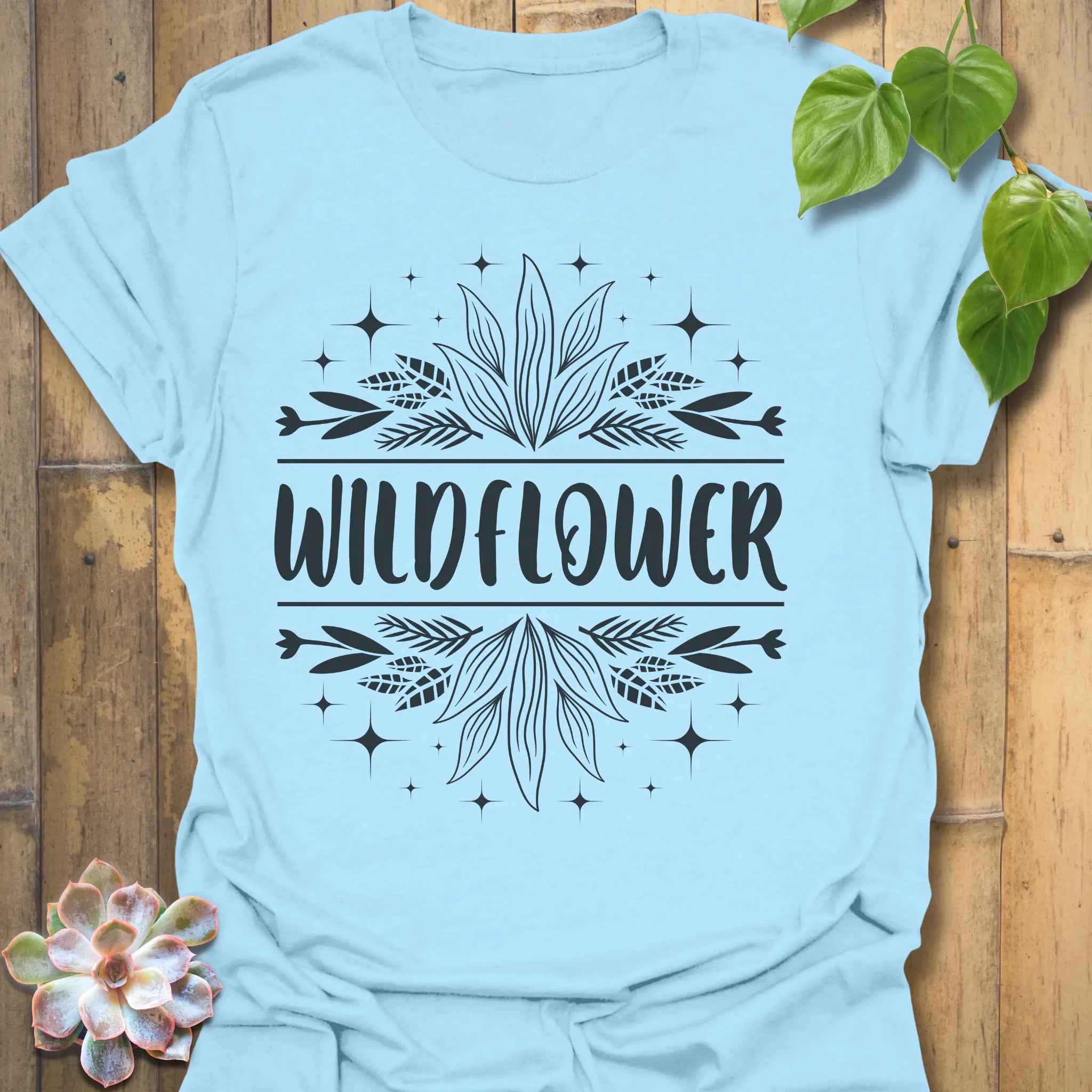 Light Blue t-shirt featuring the design Wildflower printed in bold white letters, floral graphic shirt.