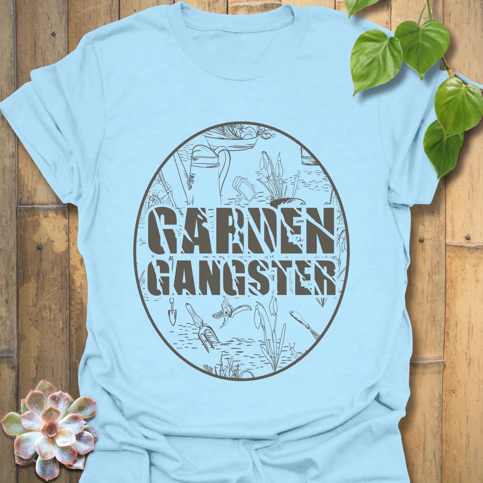 Light blue t-shirt featuring the design Garden Gangster with printed garden tools, fun gardener gift shirt with botanical style.