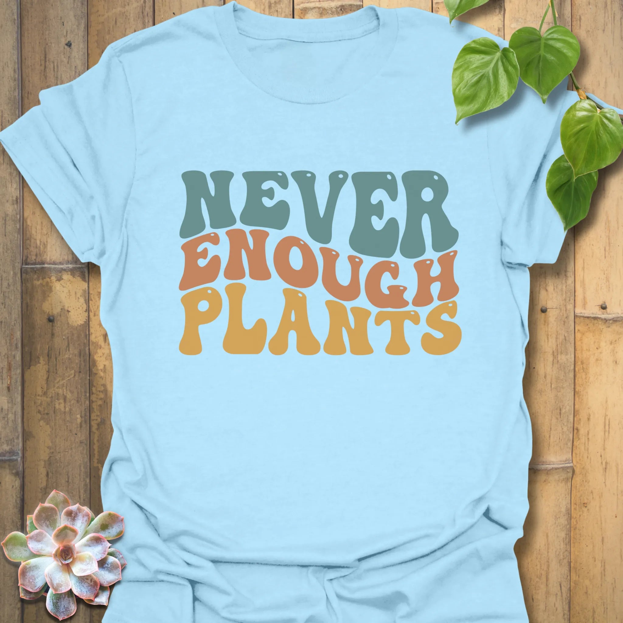 Light blue t-shirt featuring the design Never Enough Plants in bold green font with leaf graphic.