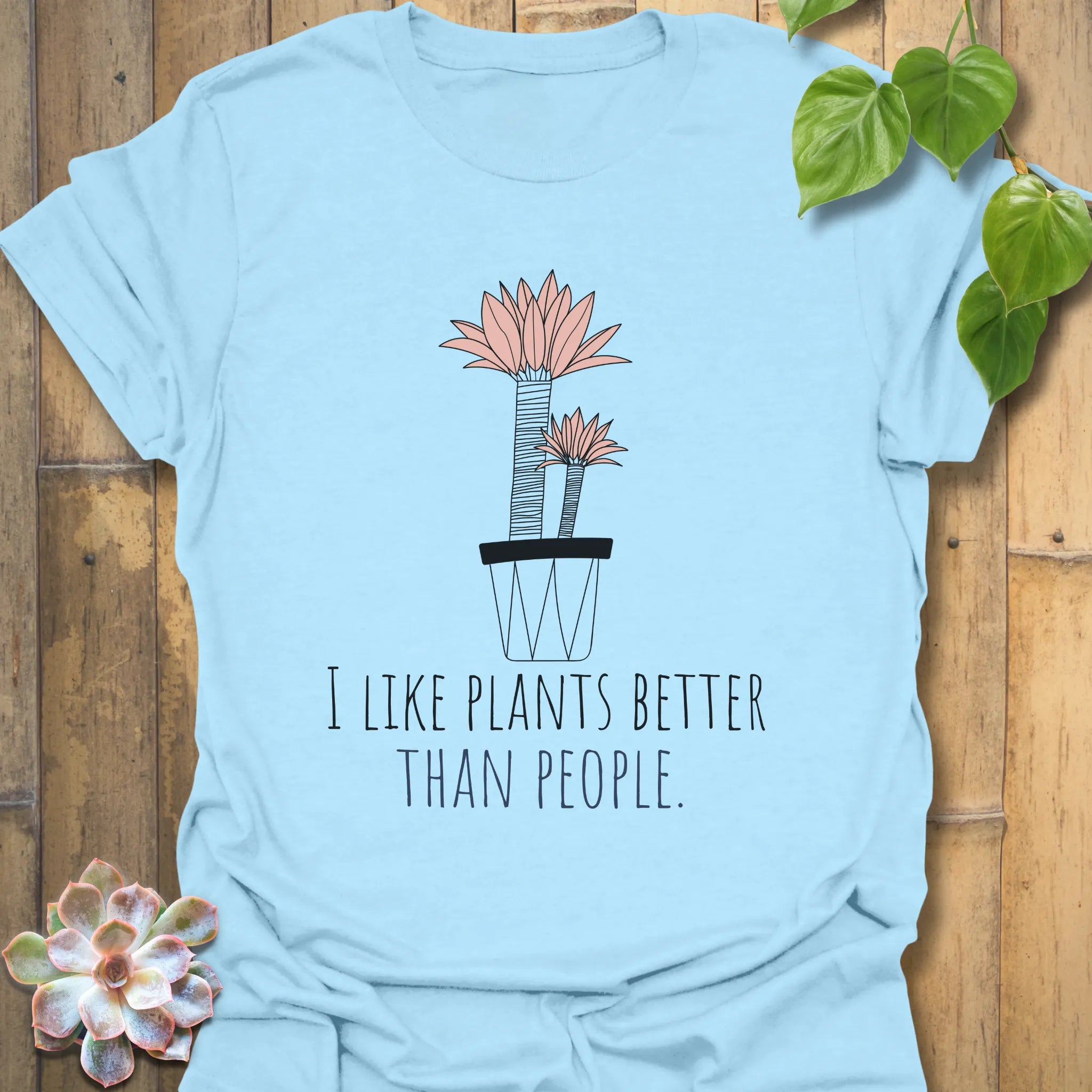 Light blue t-shirt featuring the text “I like plants better than people” with a flower in a pot artwork
