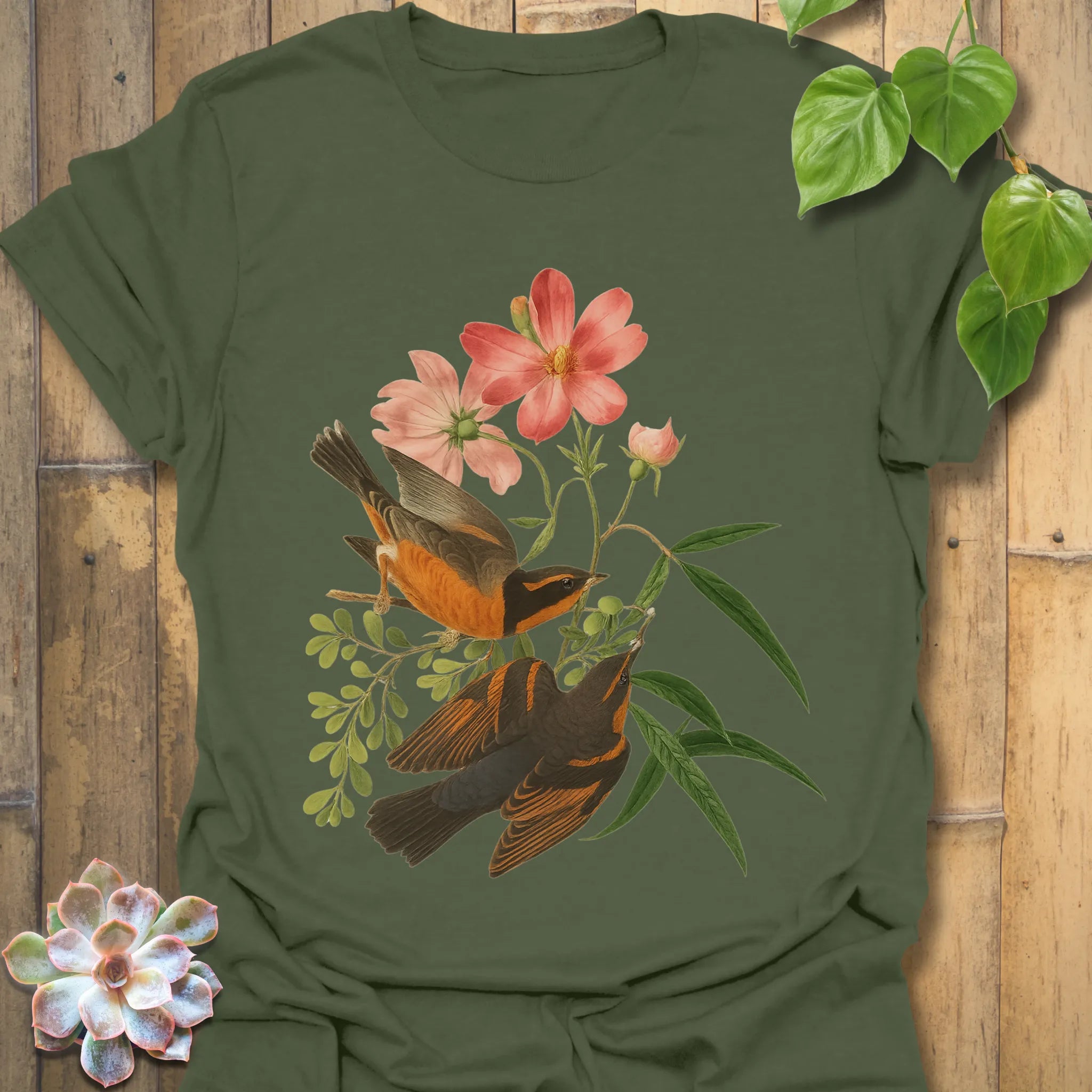 Military green t-shirt decorated with the Spring Songbirds design of two birds resting among pink flowers and leaves