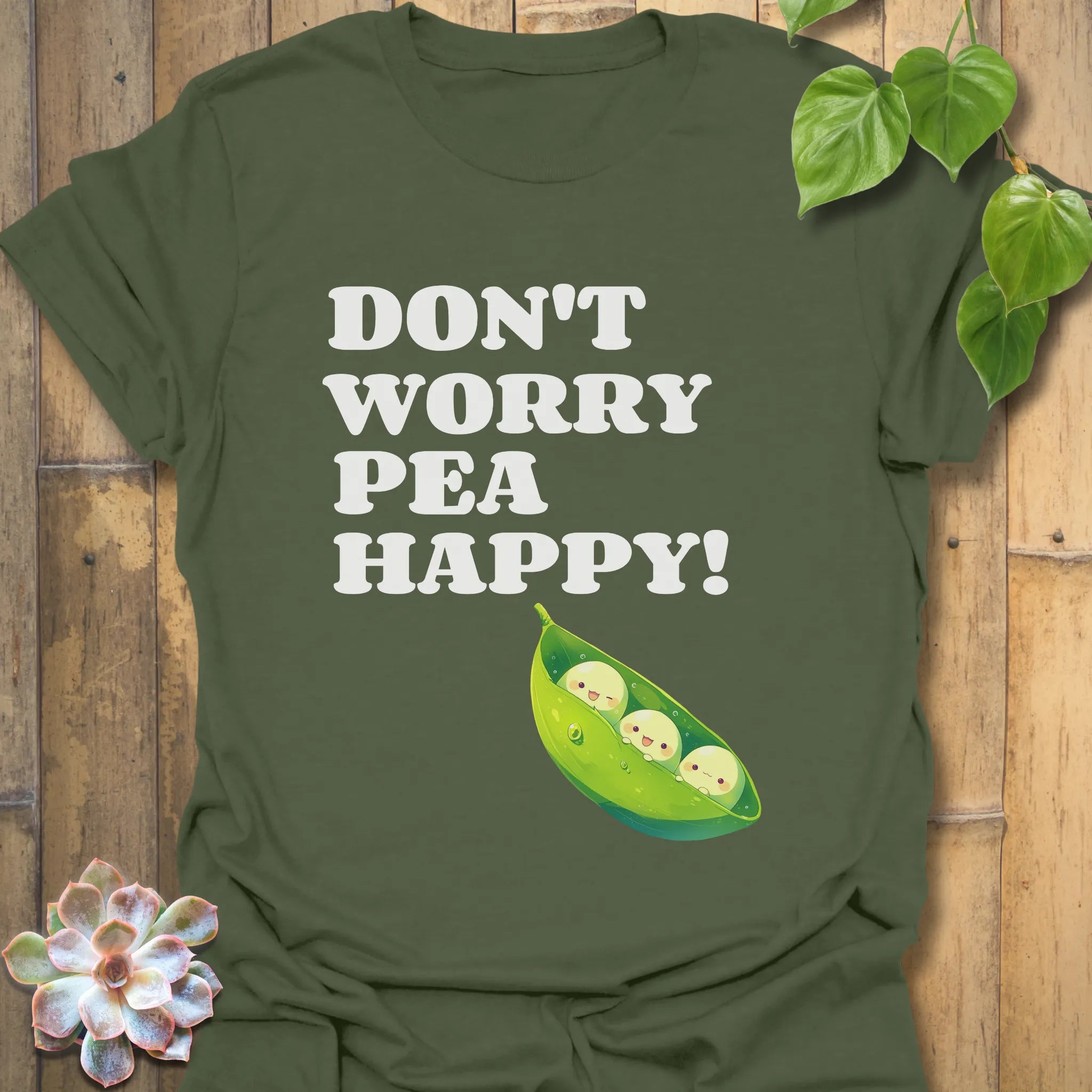 Military green t-shirt featuring the design “Don’t Worry Pea Happy” in bold white letters with three smiling peas in a pod illustration