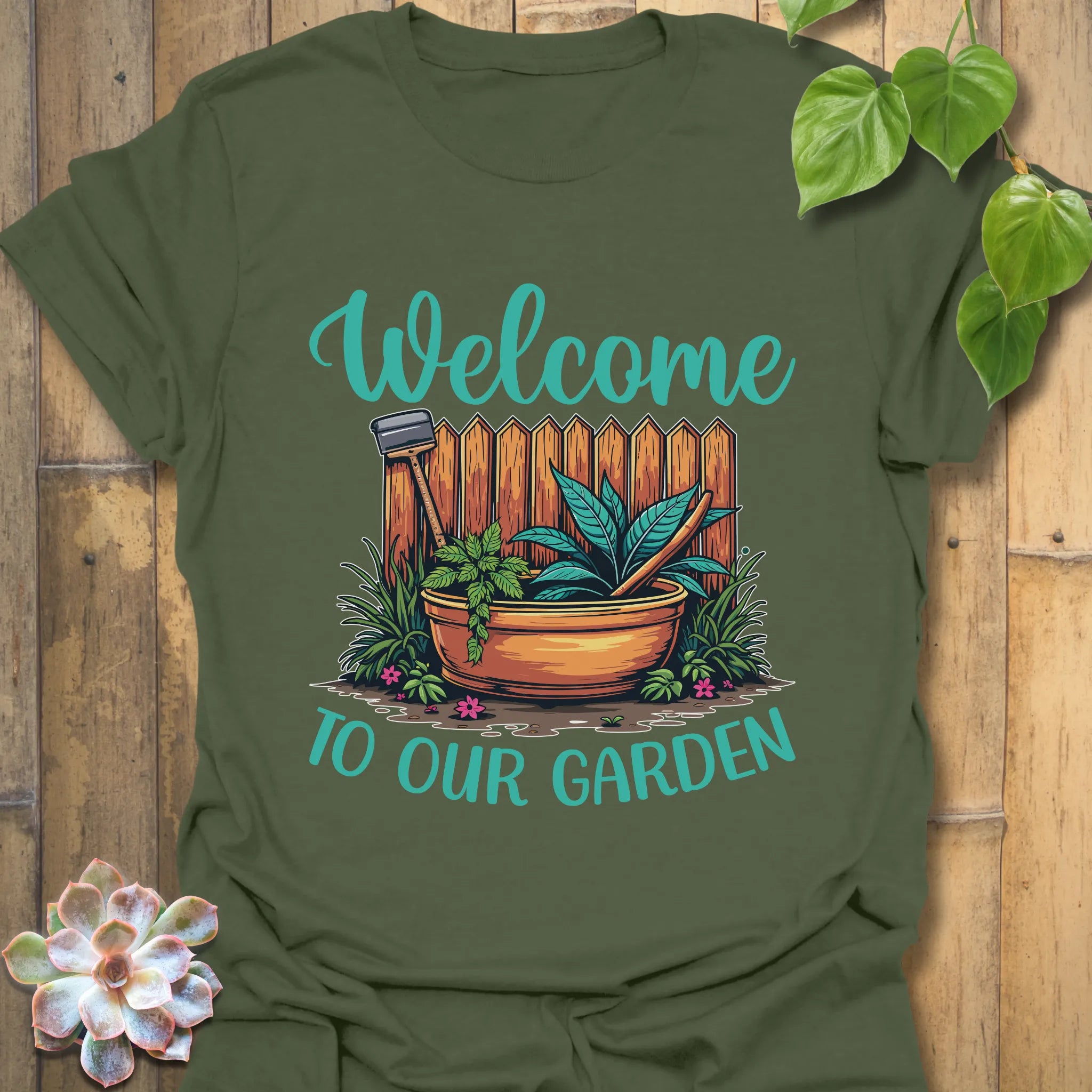 Military green t-shirt featuring the design Welcome to our garden with a garden scene, potted plant, and tools, ideal as an outdoor gardening t-shirt for nature lovers.