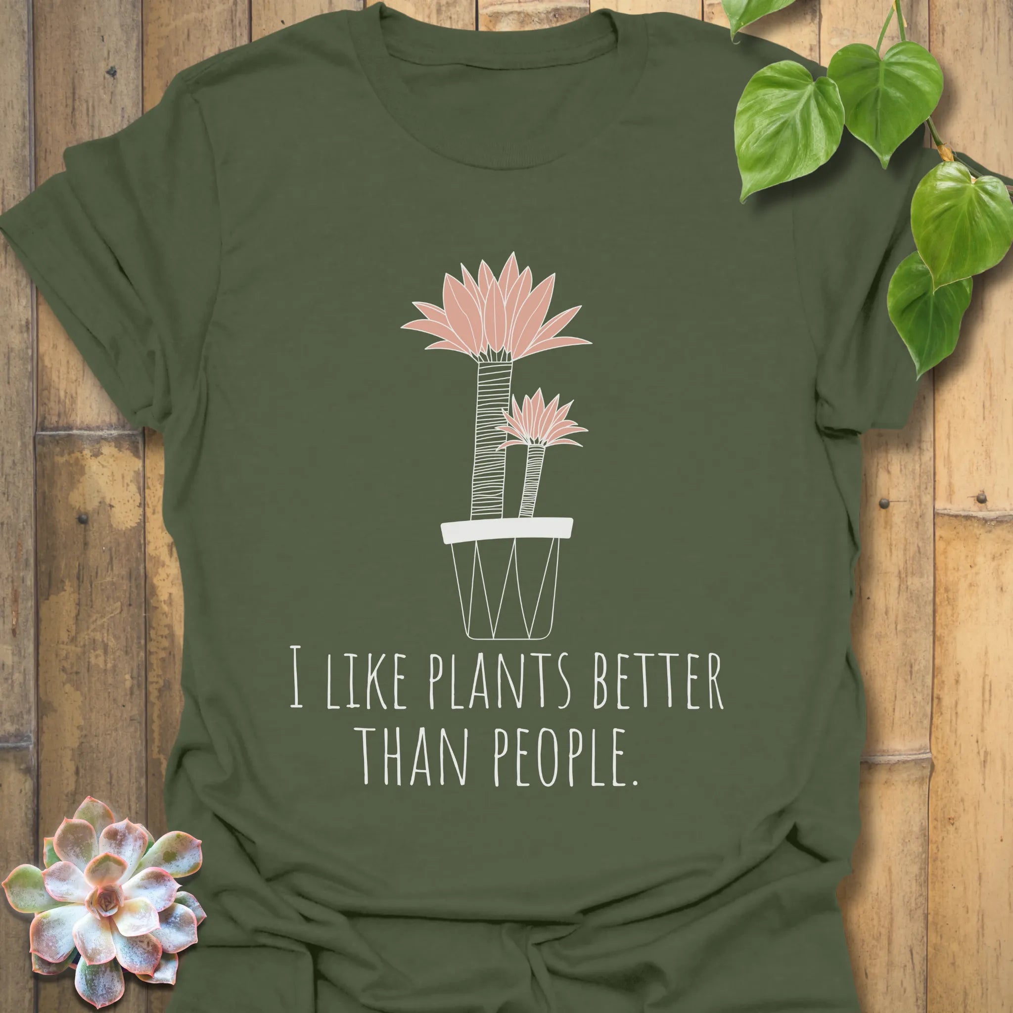 Military green t-shirt with the words “I like plants better than people” and an illustration of a flower in a pot