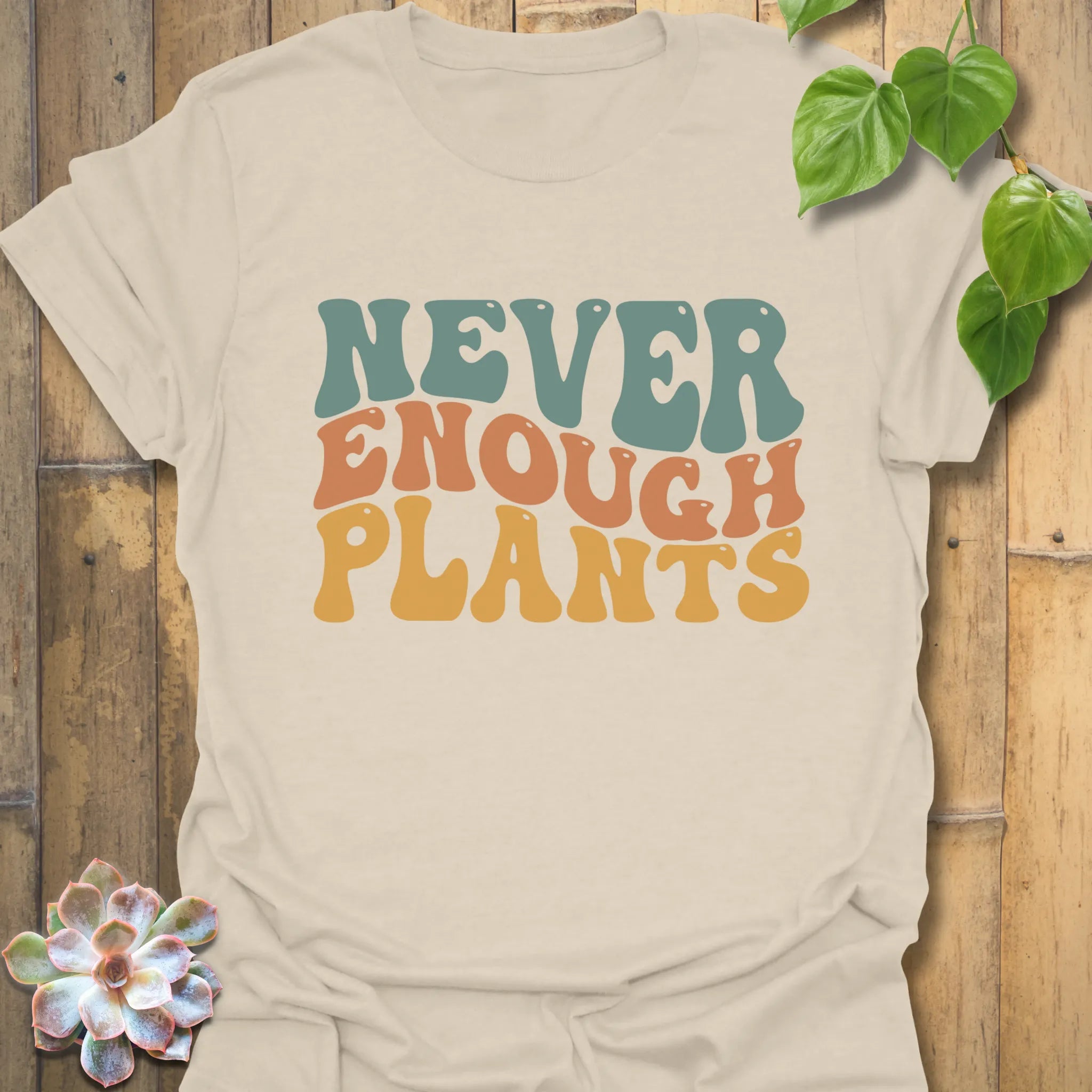 Natural beige t-shirt featuring the design Never Enough Plants in bold green lettering with leaf detail.