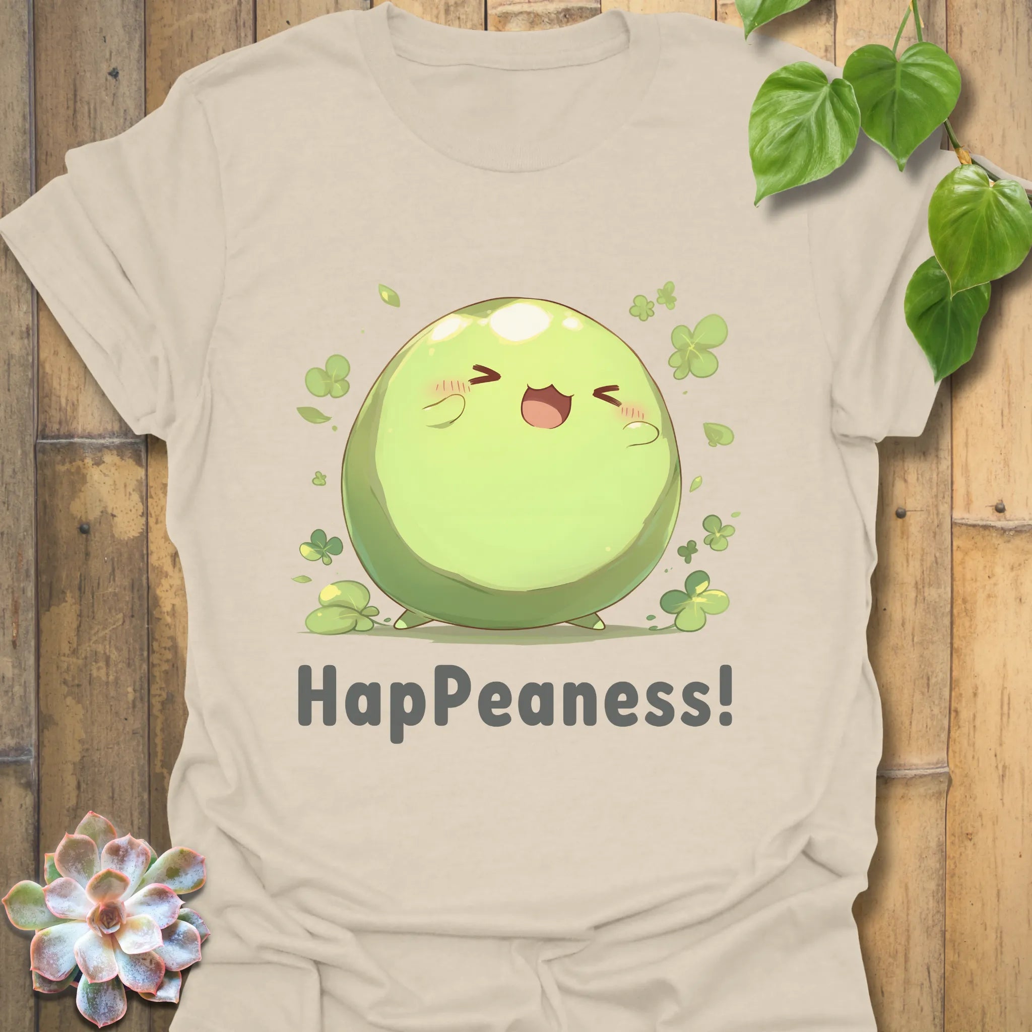 Natural colour t-shirt showing a smiling pea design with clovers and the word “HapPeaness!”