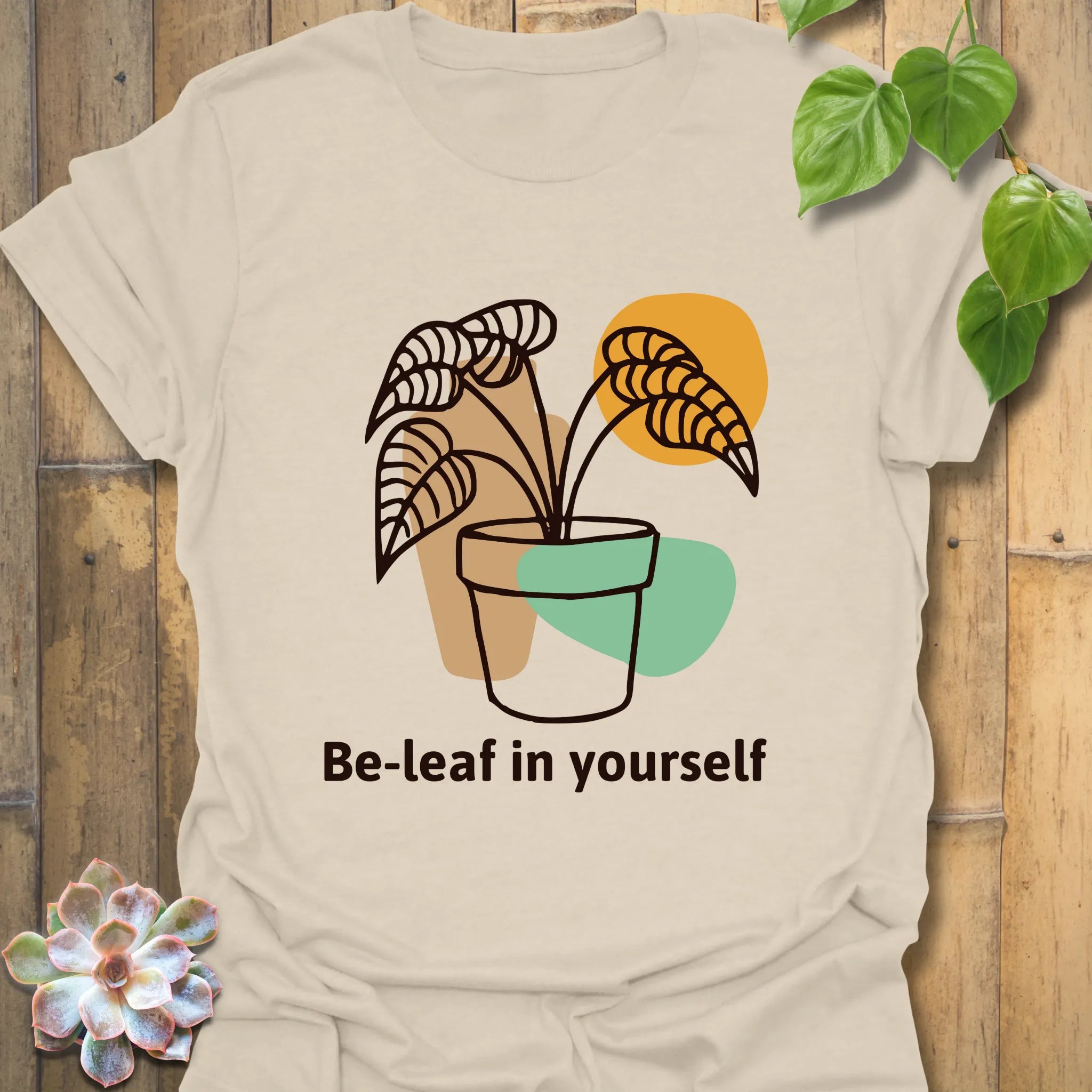 Natural colour t-shirt with the “Be-leaf in yourself” design showing a leafy potted plant illustration
