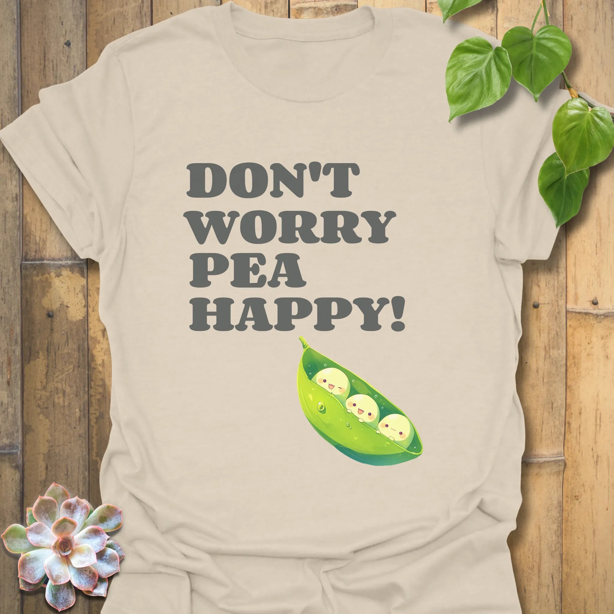 Natural t-shirt featuring the design “Don’t Worry Pea Happy” in bold green letters with three smiling peas in a pod illustration