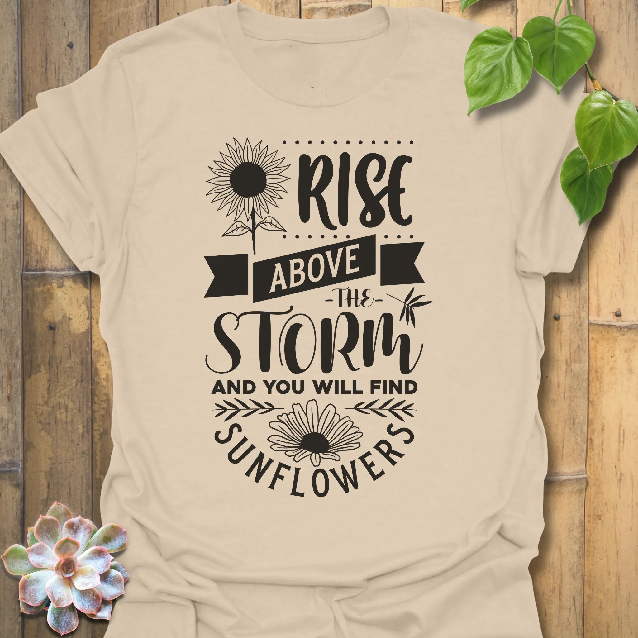Sand t-shirt featuring the design Above The Storm printed in bold letters, floral inspirational sunflower graphic shirt.