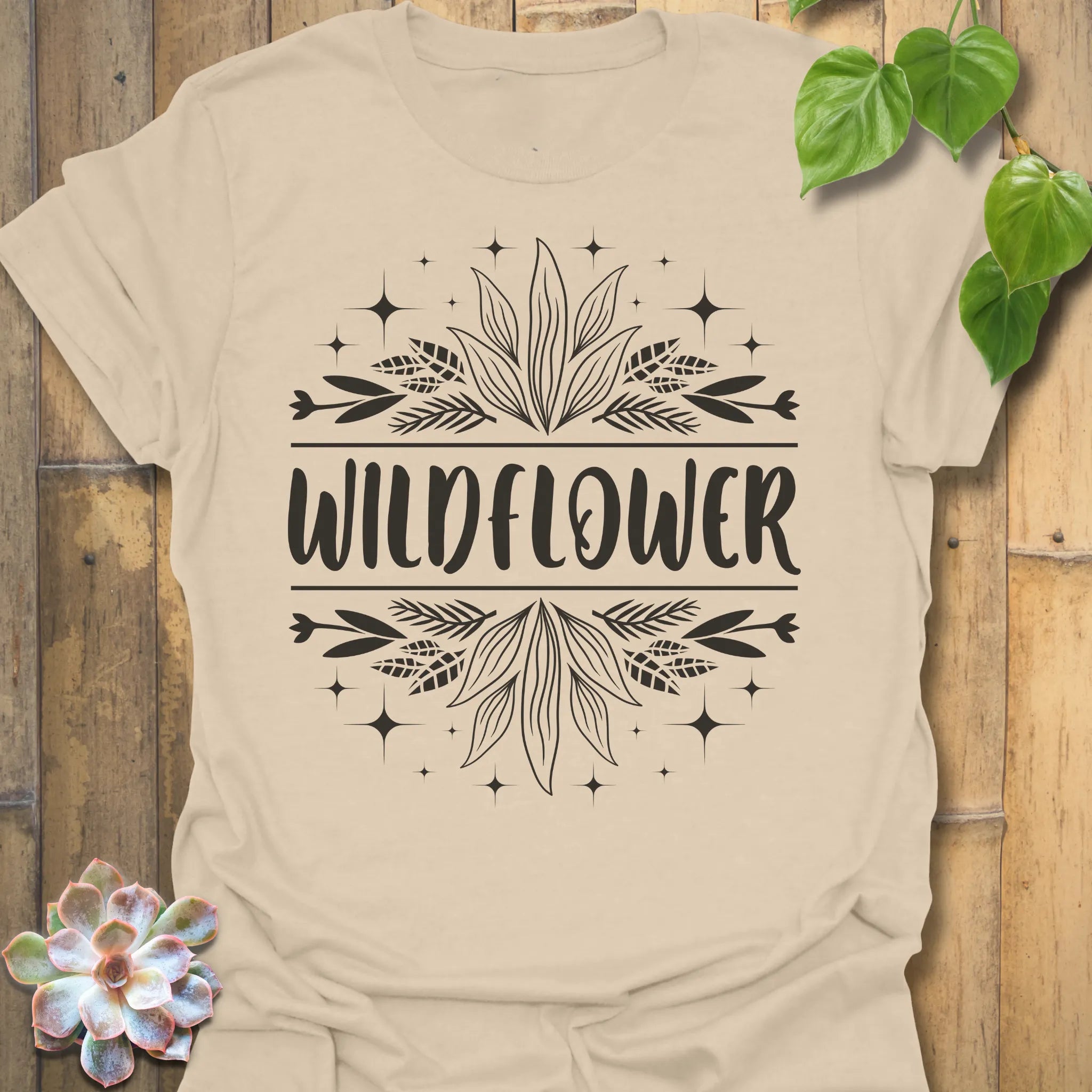 Sand t-shirt featuring the design Wildflower printed in bold white letters, floral graphic shirt.