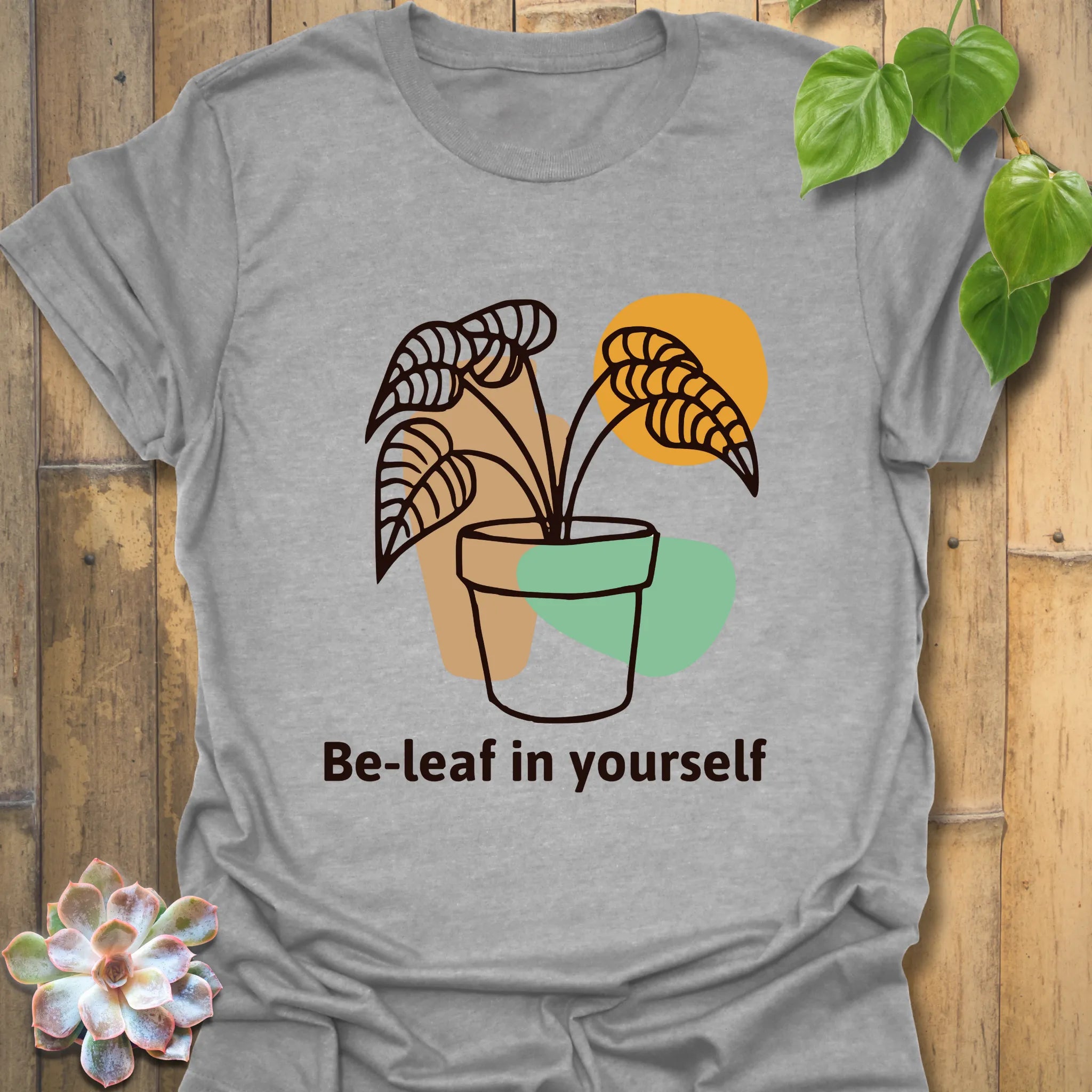 Sport grey t-shirt displaying the “Be-leaf in yourself” design with a plant in a pot