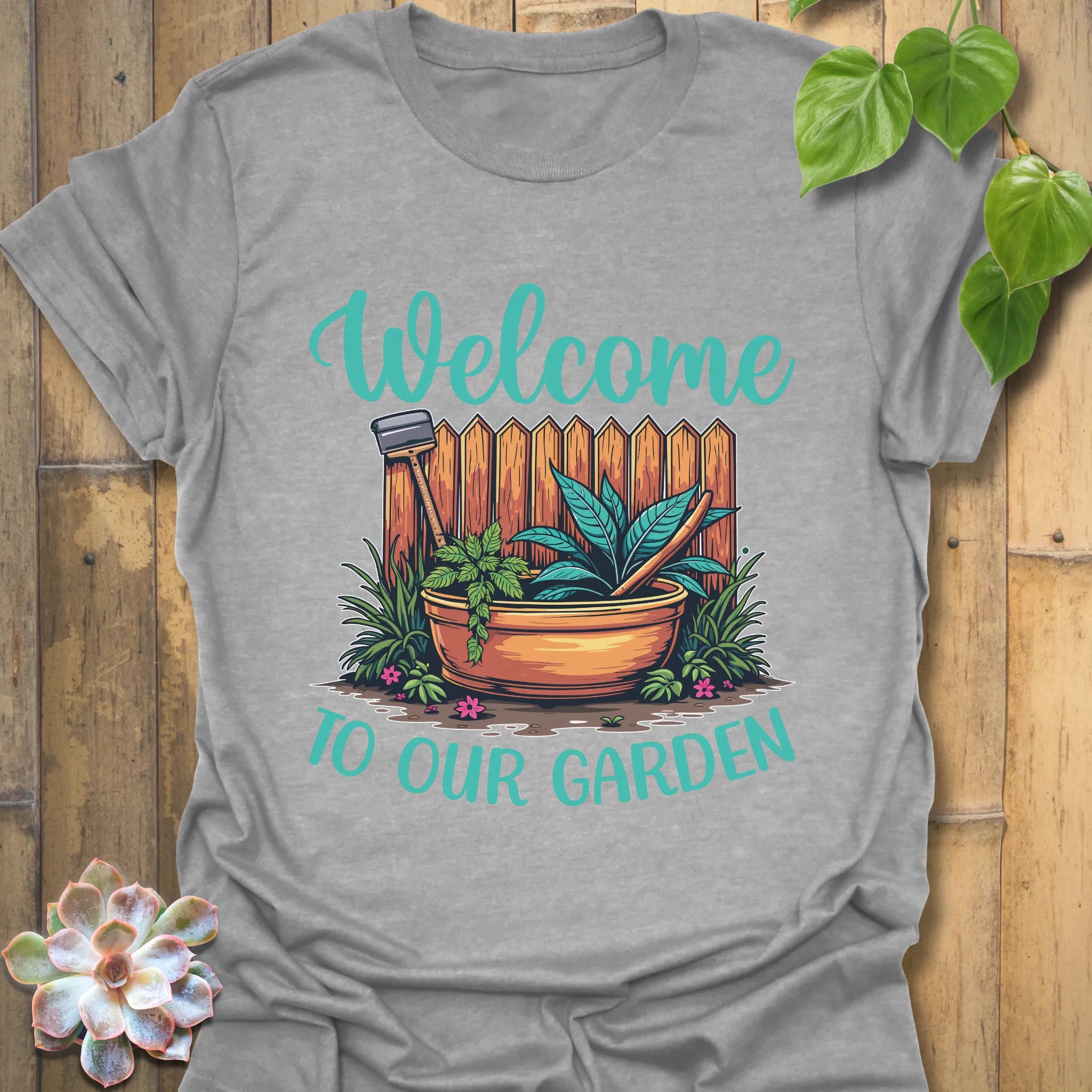 Sport grey t-shirt featuring the design Welcome to our garden with a garden scene, potted plant, and tools, a casual garden tools t-shirt perfect for plant lovers.
