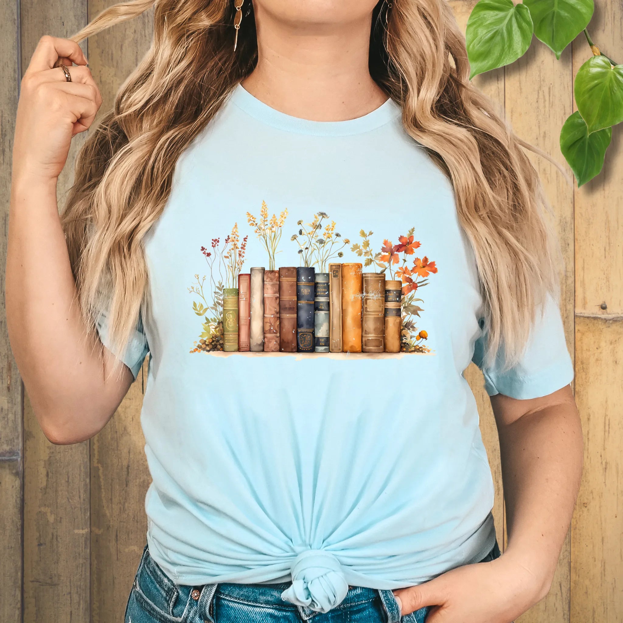 Light blue “Wildflower Library” T-shirt featuring a charming illustration of books and wildflowers, perfect for nature and book lovers.
