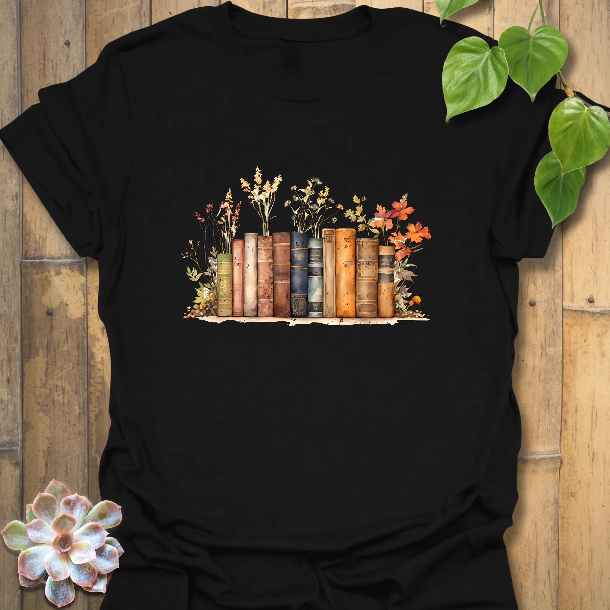 Black “Wildflower Library” T-shirt featuring a warm-toned vintage book stack surrounded by soft wildflowers — perfect for cosy readers.