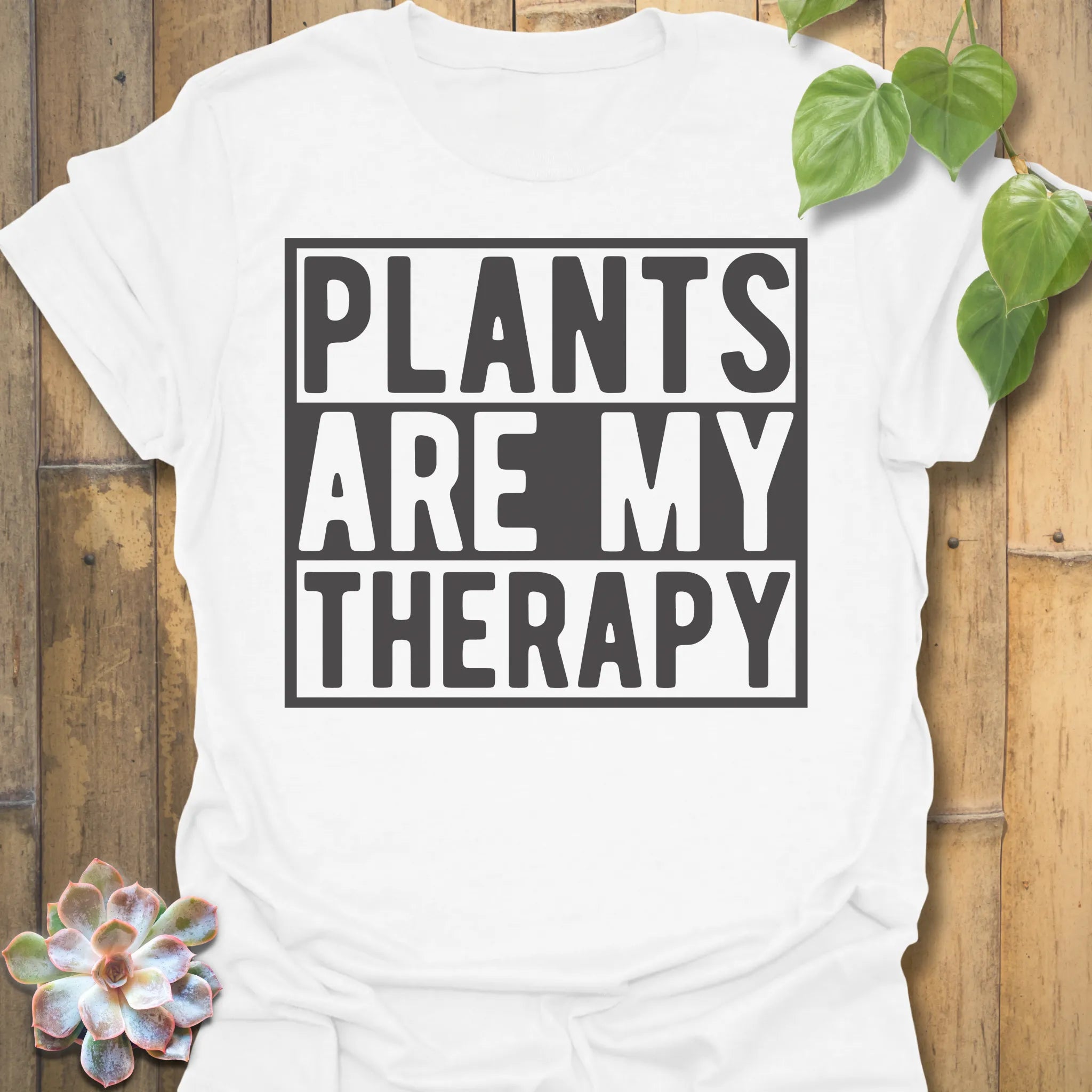 White t-shirt featuring the design Plants Are My Therapy printed in bold letters, plant lover shirt.