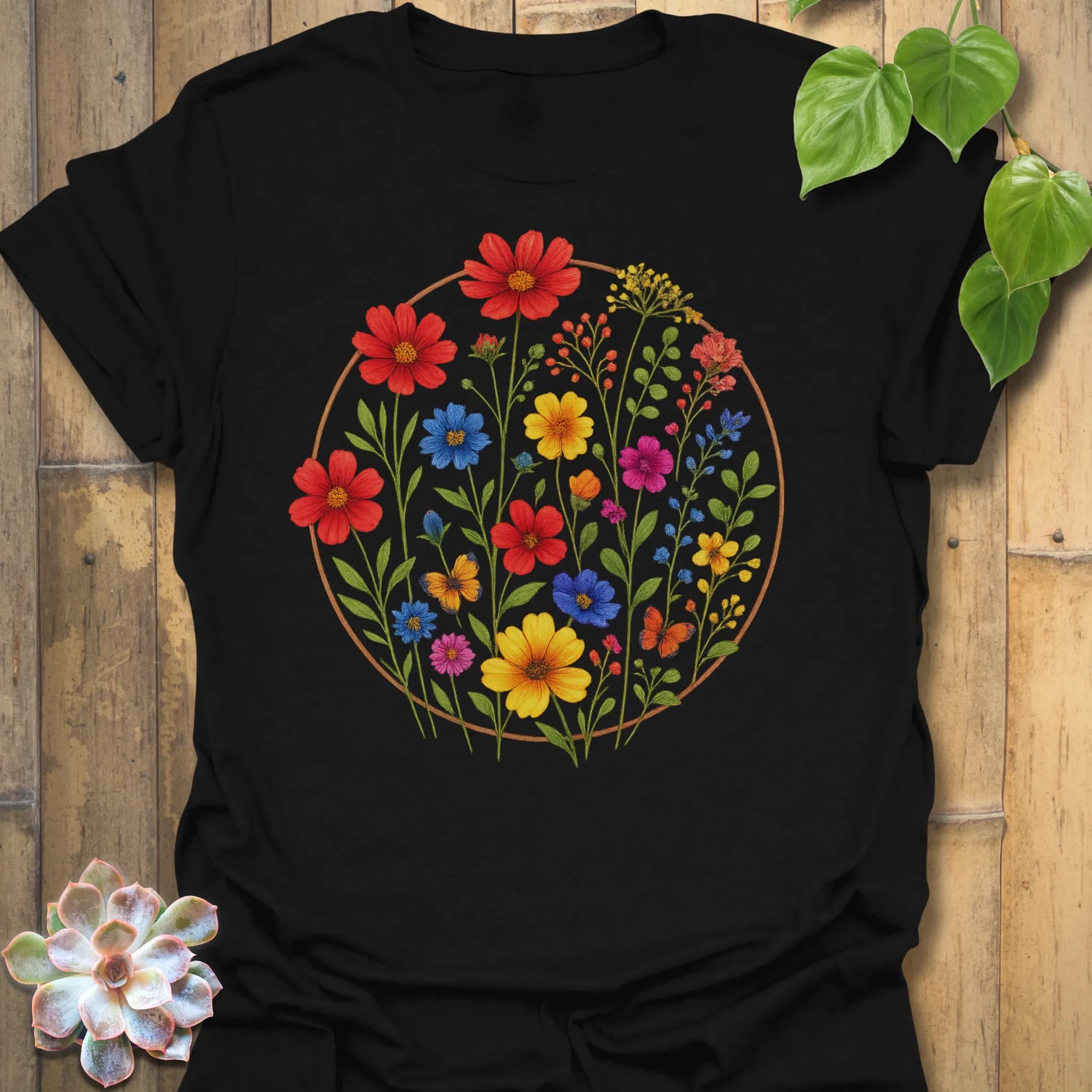Black “Circle of Flowers” T-shirt with a bright circular wildflower design in red, yellow, blue, and pink tones — vibrant nature-inspired print on Gildan 64000.