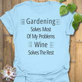 Gildan 64000 Light Blue unisex t-shirt displaying the phrase ‘Gardening solves most of my problems, wine solves the rest’ in white text. Soft cotton blend.