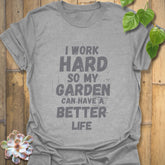Sport grey unisex T-shirt featuring large white distressed typography that says “I work hard so my garden can have a better life,” laid flat on rustic wood with a small succulent beside it.