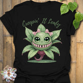 Black t-shirt featuring the design Creepin’ It Leafy printed in bold black letters, gardening graphic shirt.