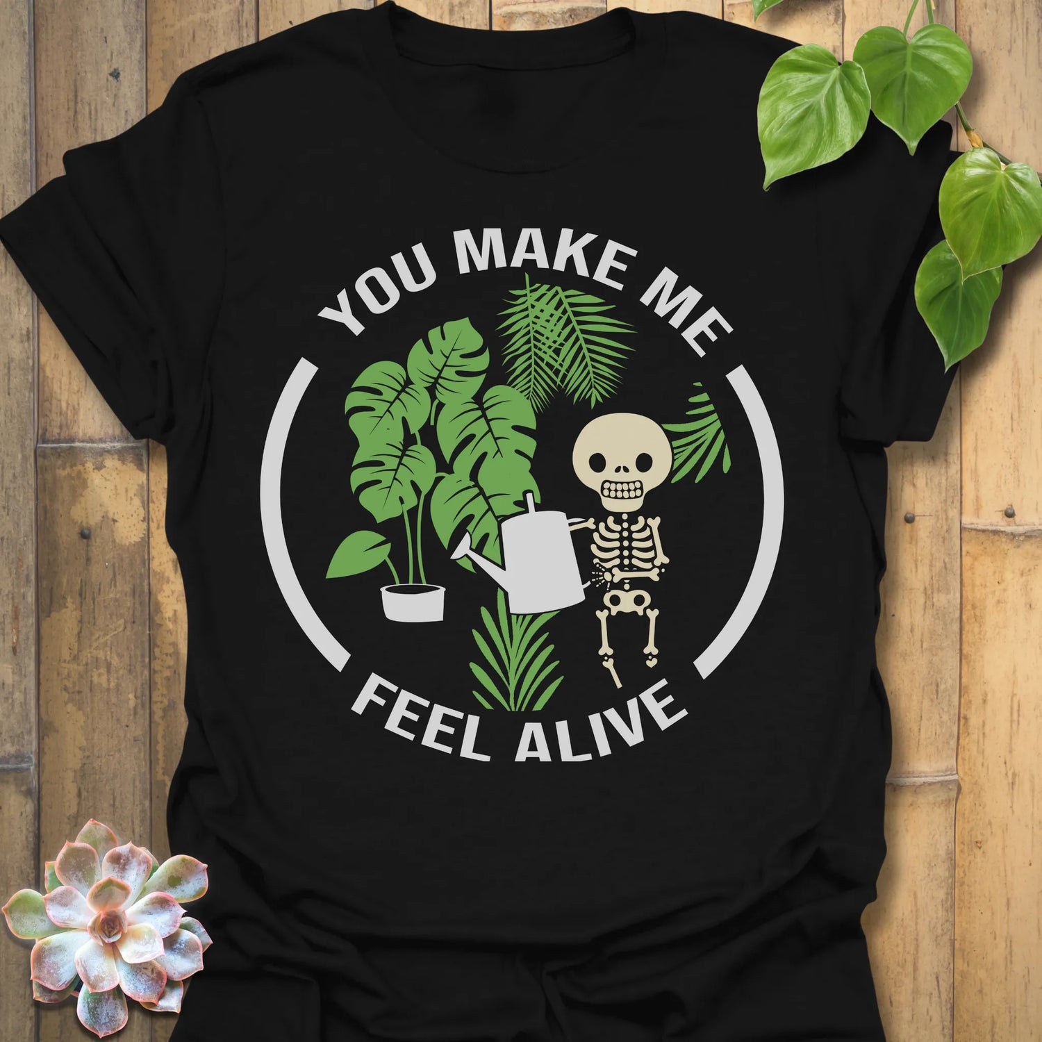 Black t-shirt featuring the design Feel Alive printed in bold white letters with plants, motivational graphic tee.
