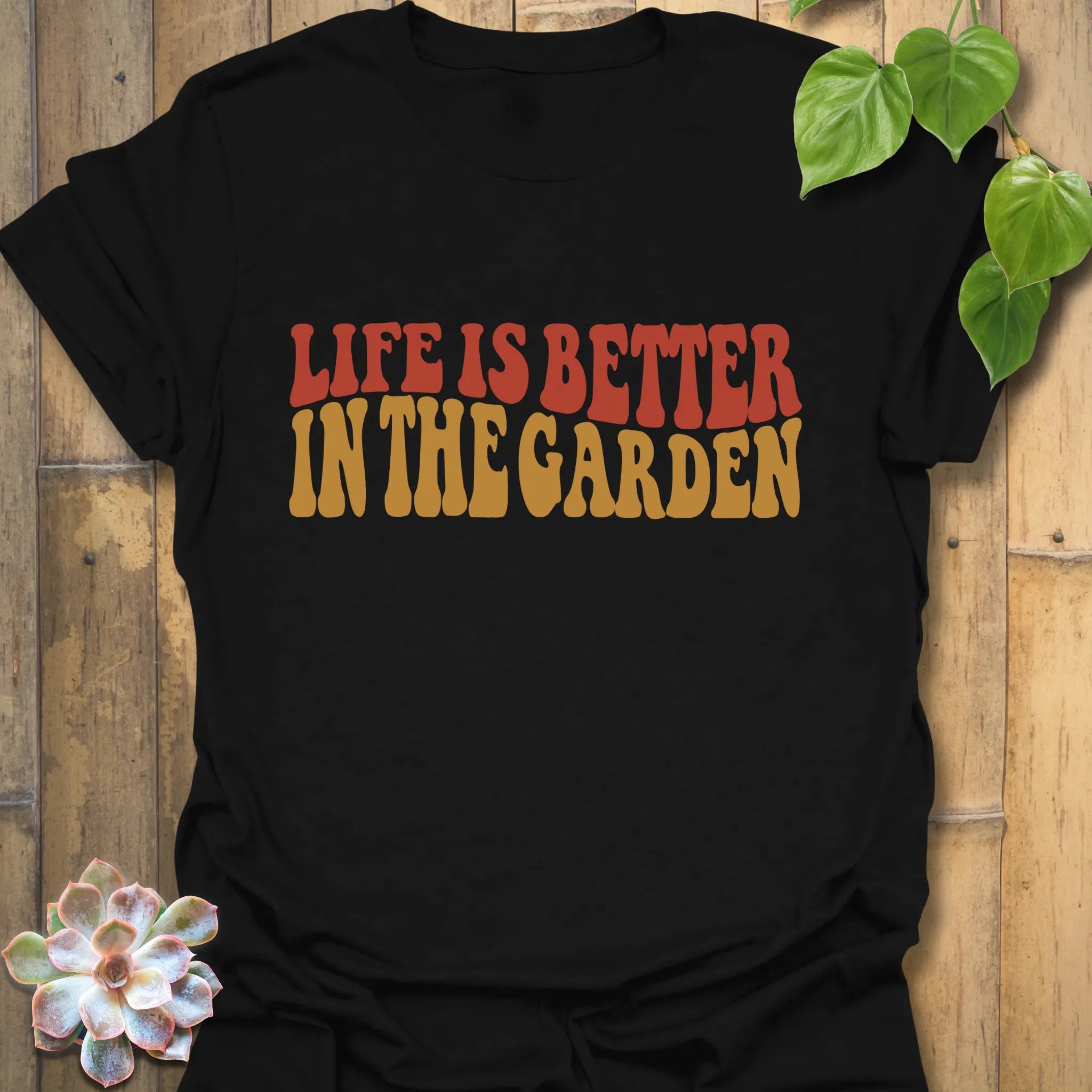 Black t-shirt featuring the design Life is better in the garden printed in green floral lettering, modern plant lover and gardening shirt