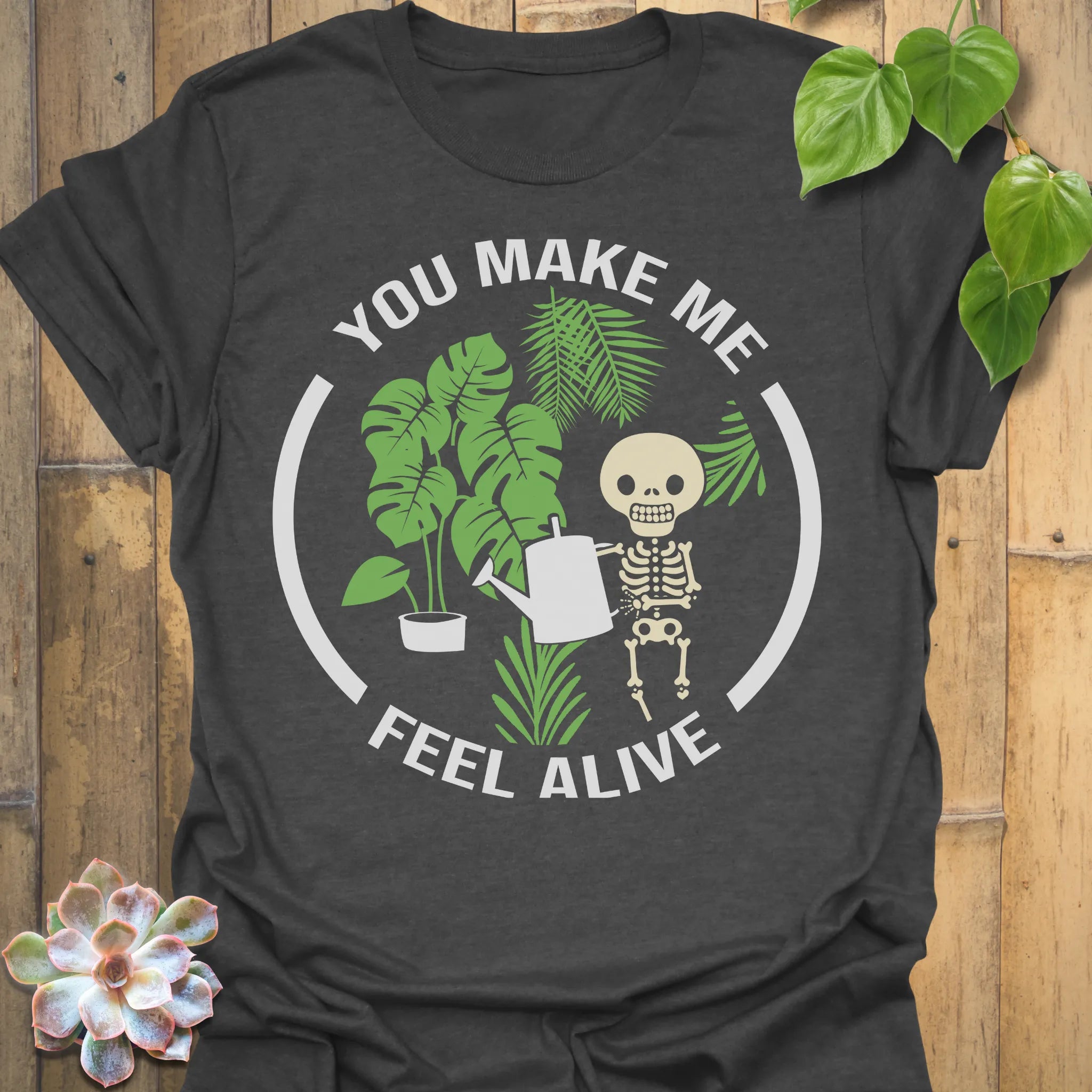 Dark Heather t-shirt featuring the design Feel Alive printed in bold white letters with plants, motivational graphic tee.