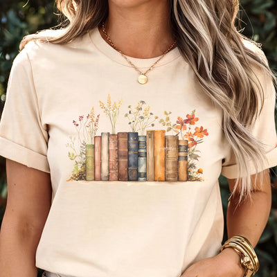 Natural “Wildflower Library” T-shirt featuring a vintage stack of books with wildflowers blooming around them, printed on soft Gildan 64000 cotton.