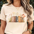 Natural “Wildflower Library” T-shirt featuring a vintage stack of books with wildflowers blooming around them, printed on soft Gildan 64000 cotton.