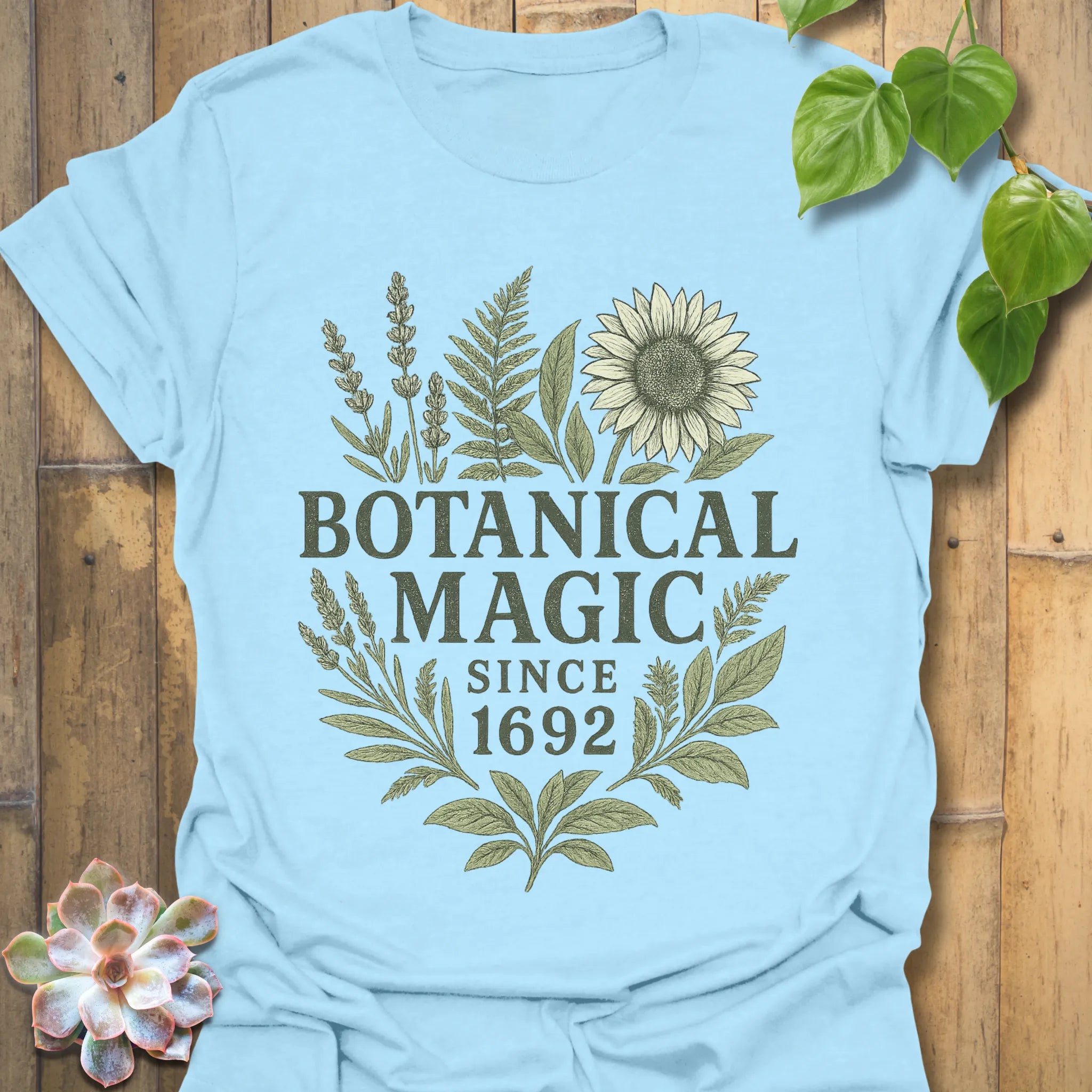 Light Blue t-shirt featuring the design Botanical Magic printed in bold letters, floral graphic tee.