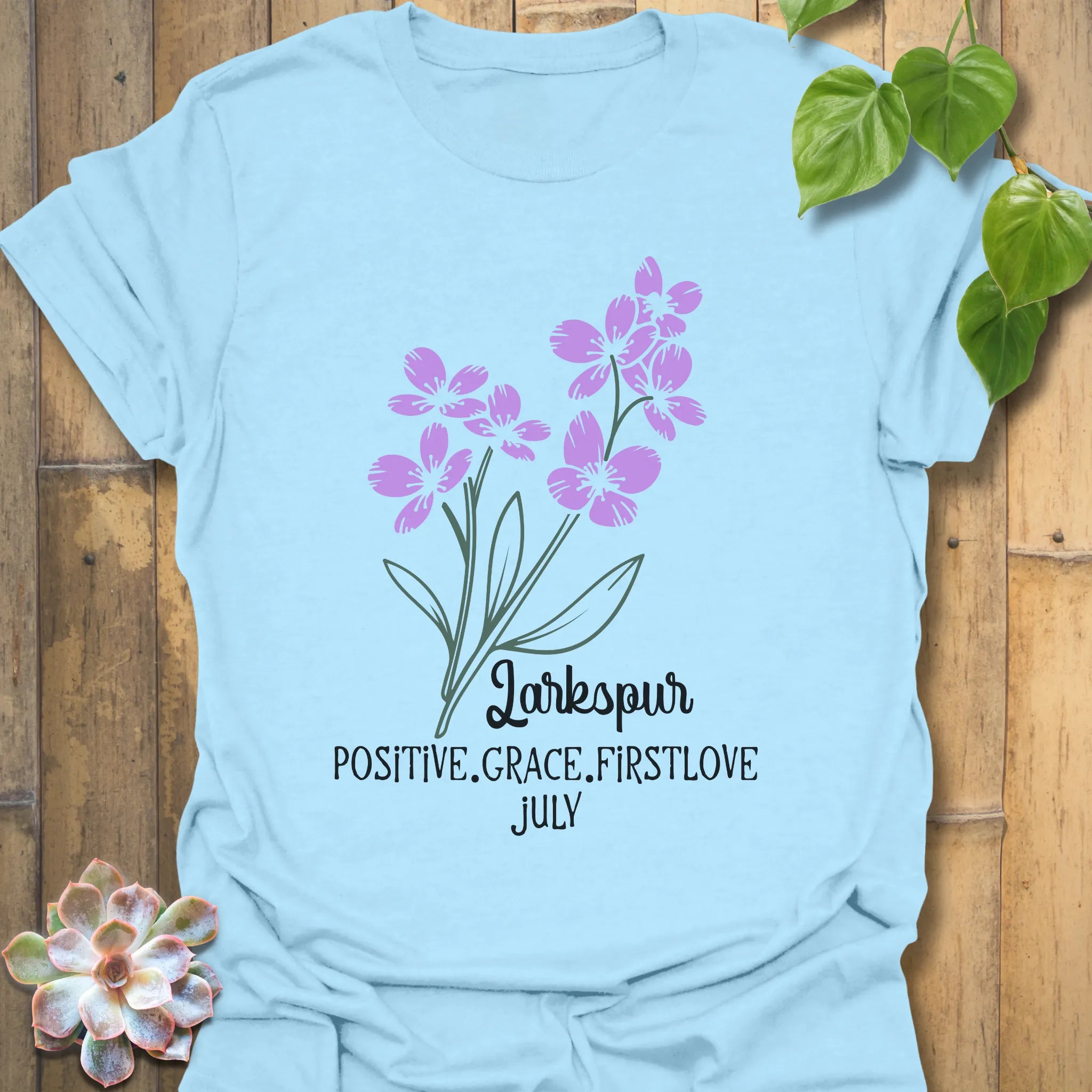 Light Blue t-shirt featuring the design July Larkspur with a soft larkspur flower graphic, making it a stylish floral print tee for garden-inspired fashion and summer outfits.