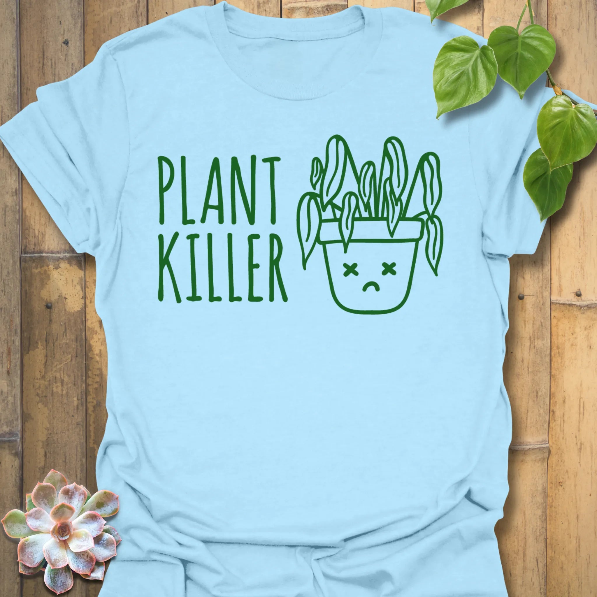 Light Blue t-shirt featuring the design Plant Killer printed in bold green letters, funny plant lover shirt.