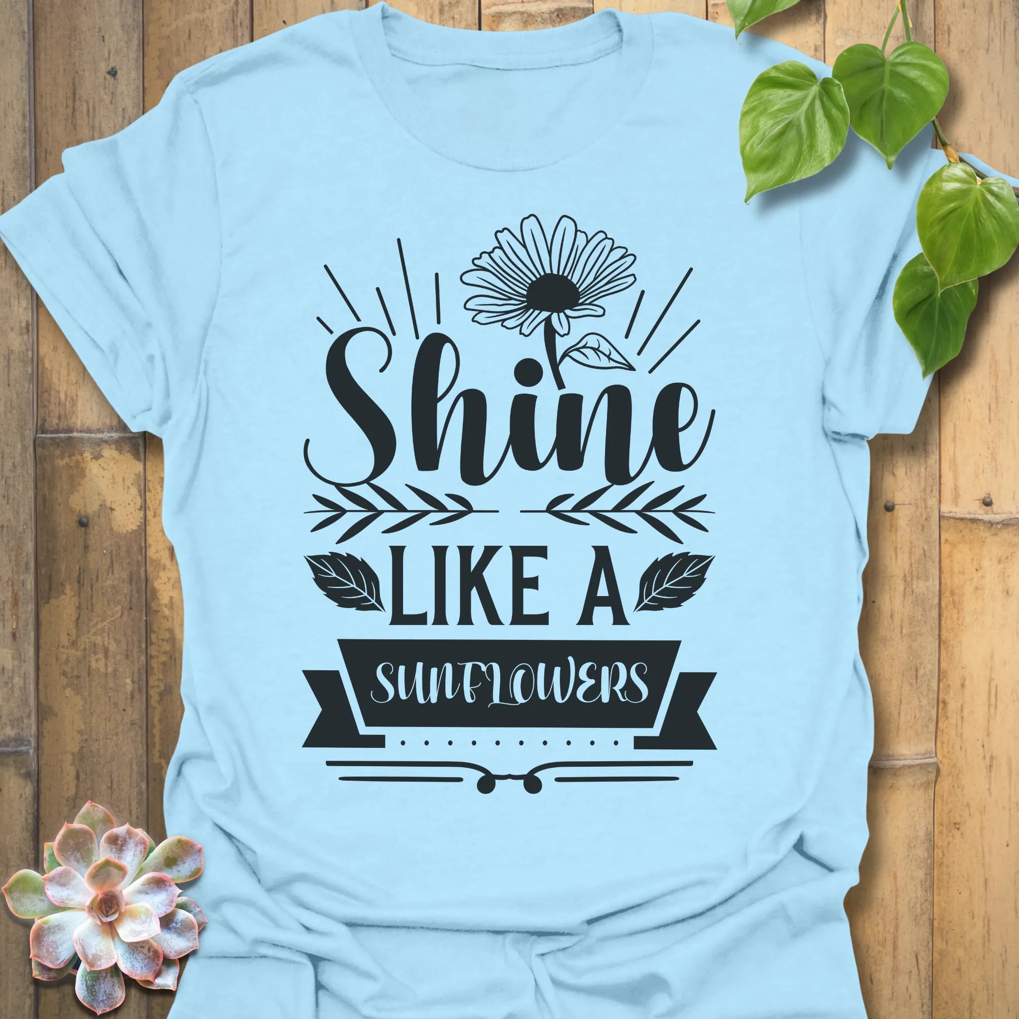 Light Blue t-shirt featuring the design Shine Like A Sunflower printed in bold letters, sunflower lover shirt.