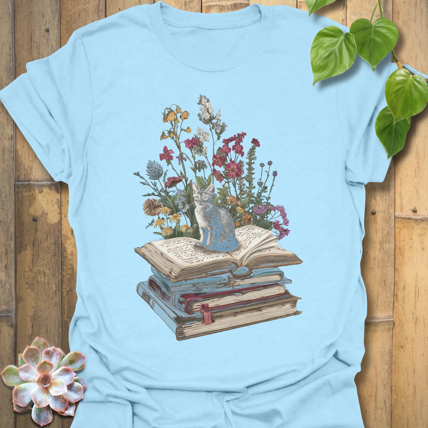 Light Blue t-shirt featuring the design Whiskers &amp; Words printed in books and cats with flowers, cat lover reading shirt.