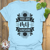 Light Blue t-shirt featuring the design You Are My Sunshine printed in bold letters, nature-inspired graphic tee.